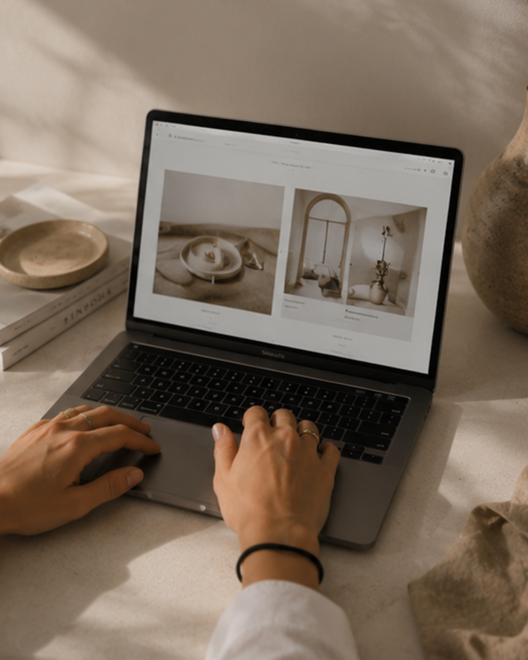 Persona usando una laptop en una mesa con decoraciones en tonos neutros, visualizando una página web con fotos de artículos decorativos y cerámicas.
