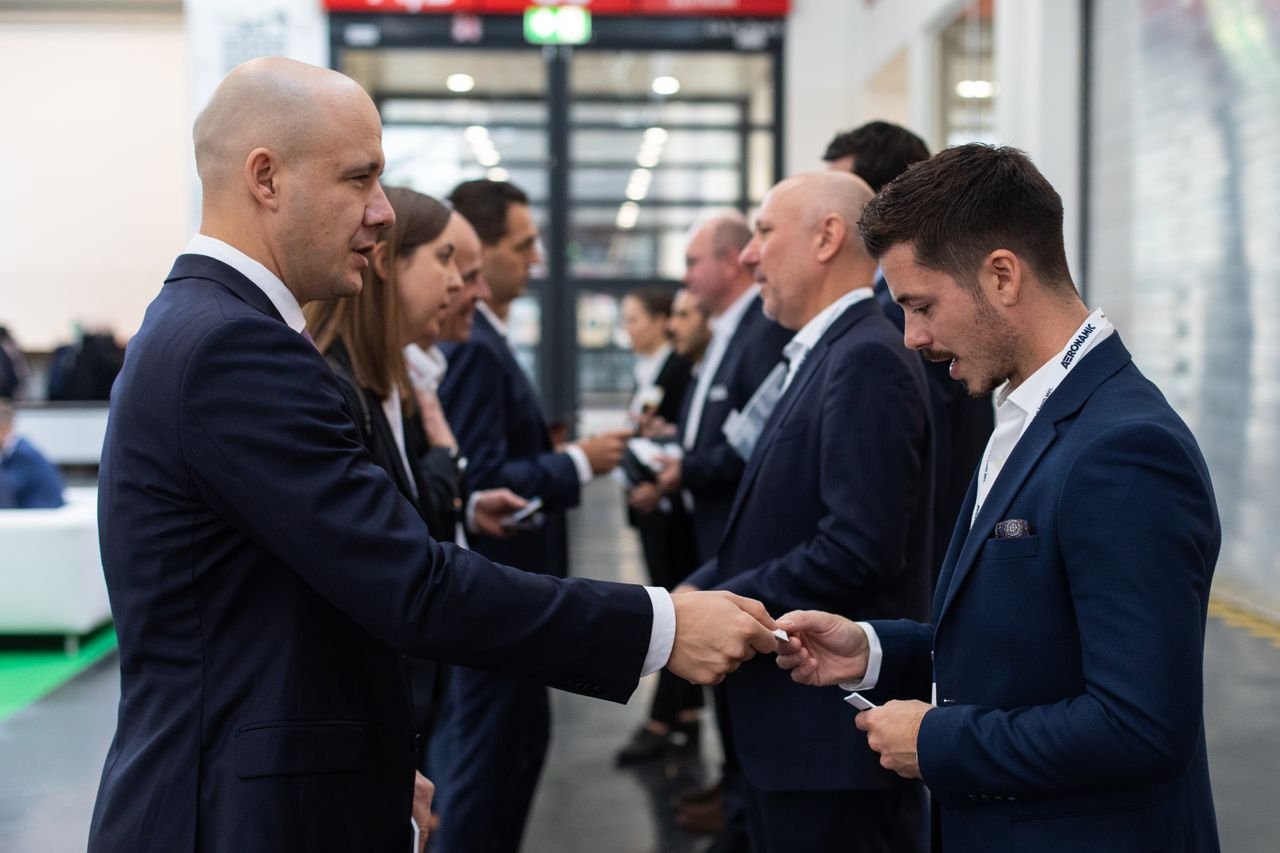 A group of business professionals dressed in suits standing in a line at an event, exchanging business cards.
