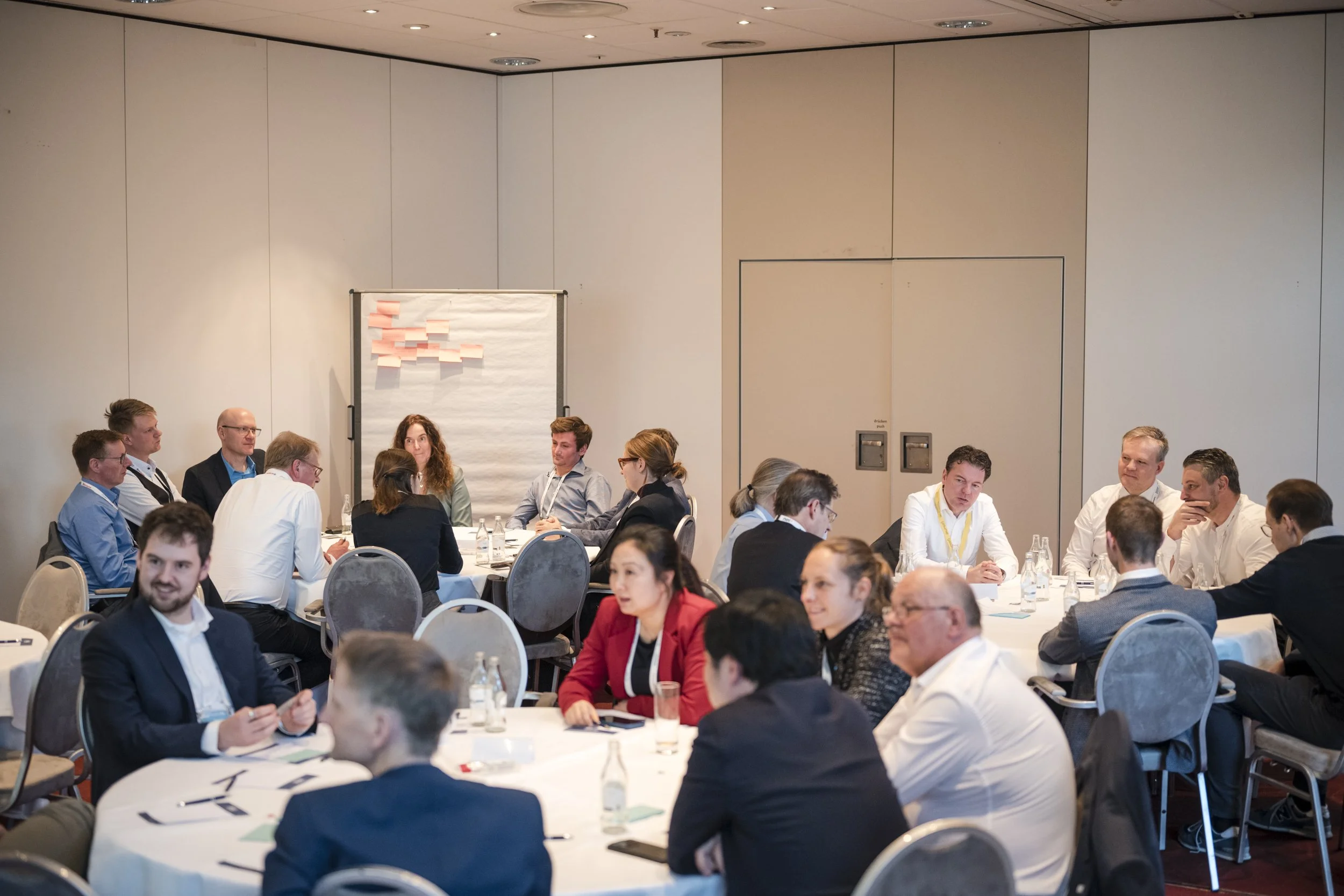 Gruppendiskussion bei einer Konferenz mit mehreren Menschen, die an runden Tischen sitzen, in einem großen Konferenzraum.