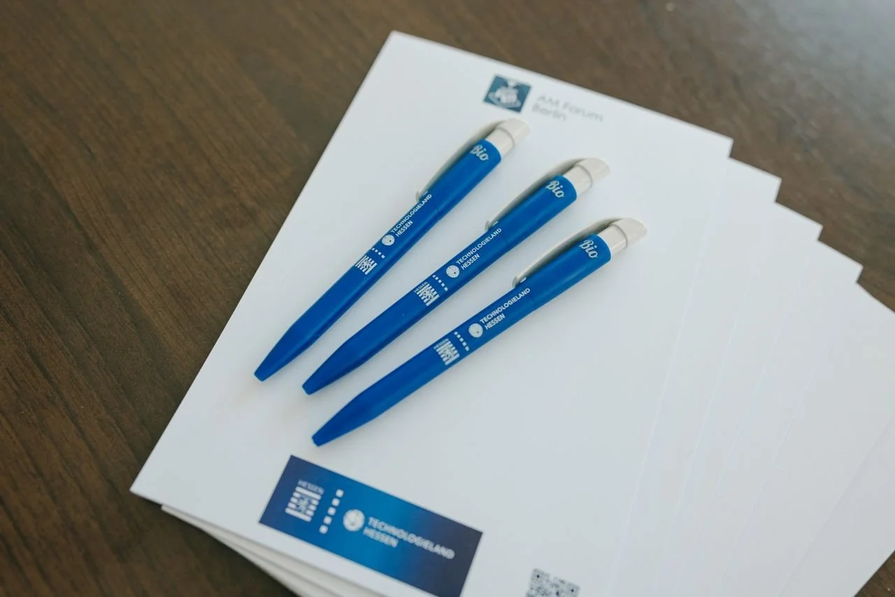 Drei blaue Kugelschreiber auf weißen Papieren mit dem Logo und Text "TECHNOLOGIELAND HESSEN".