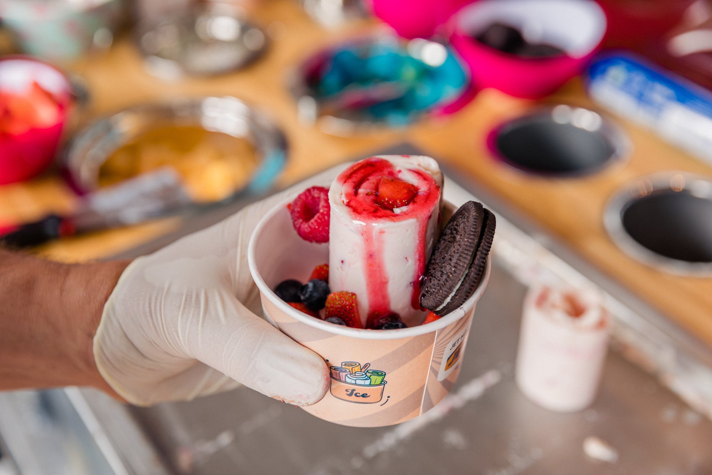 Hand hält Becher mit Eiscreme, umgeben von Beeren und Oreo-Keks.