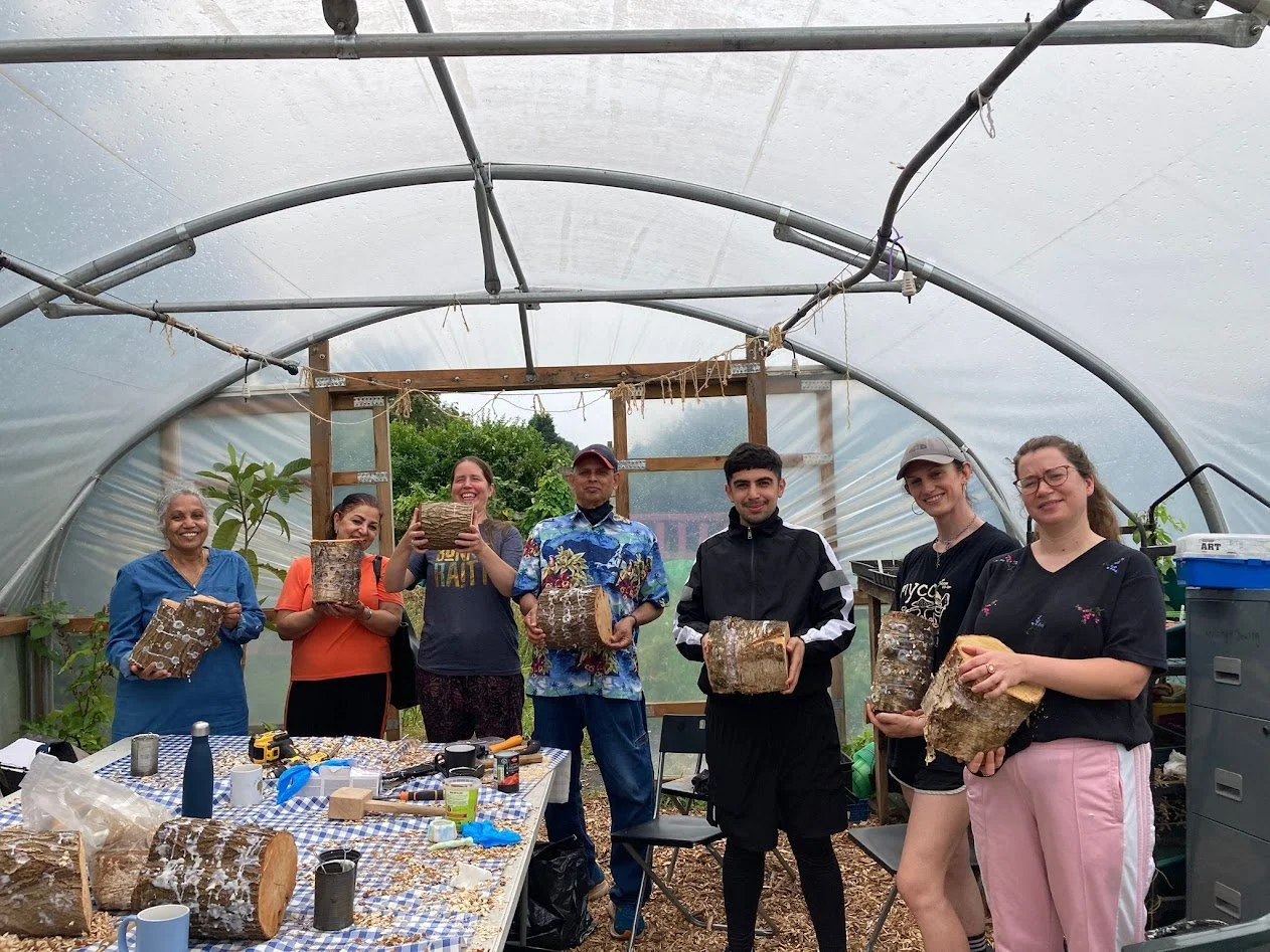 A group of adults stand together in a bright polytunnel holding logs