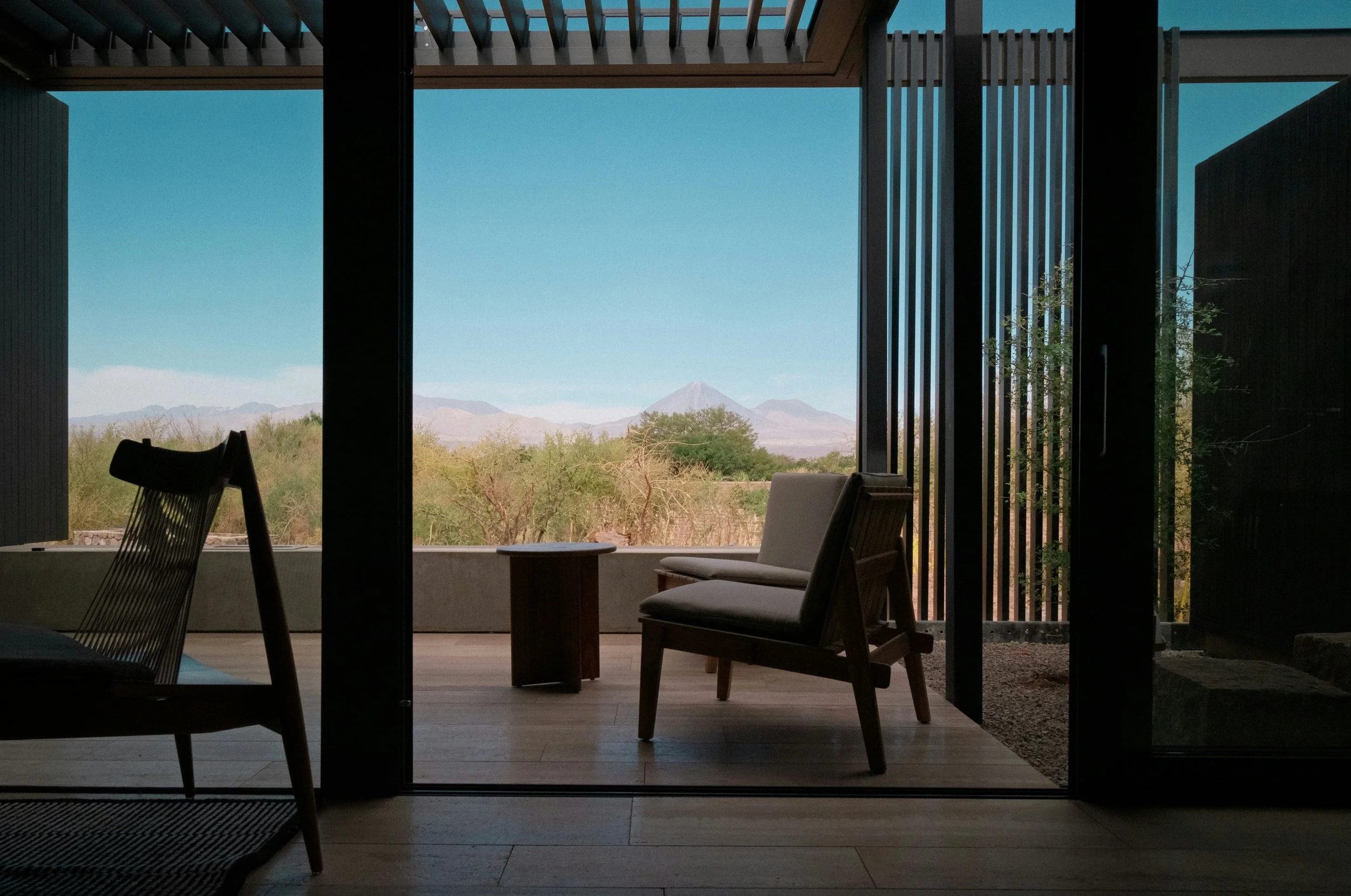 Vue depuis une salle intérieure vers l'extérieur, montrant un paysage désertique avec des montagnes au loin et un ciel clair, à travers de grandes fenêtres.