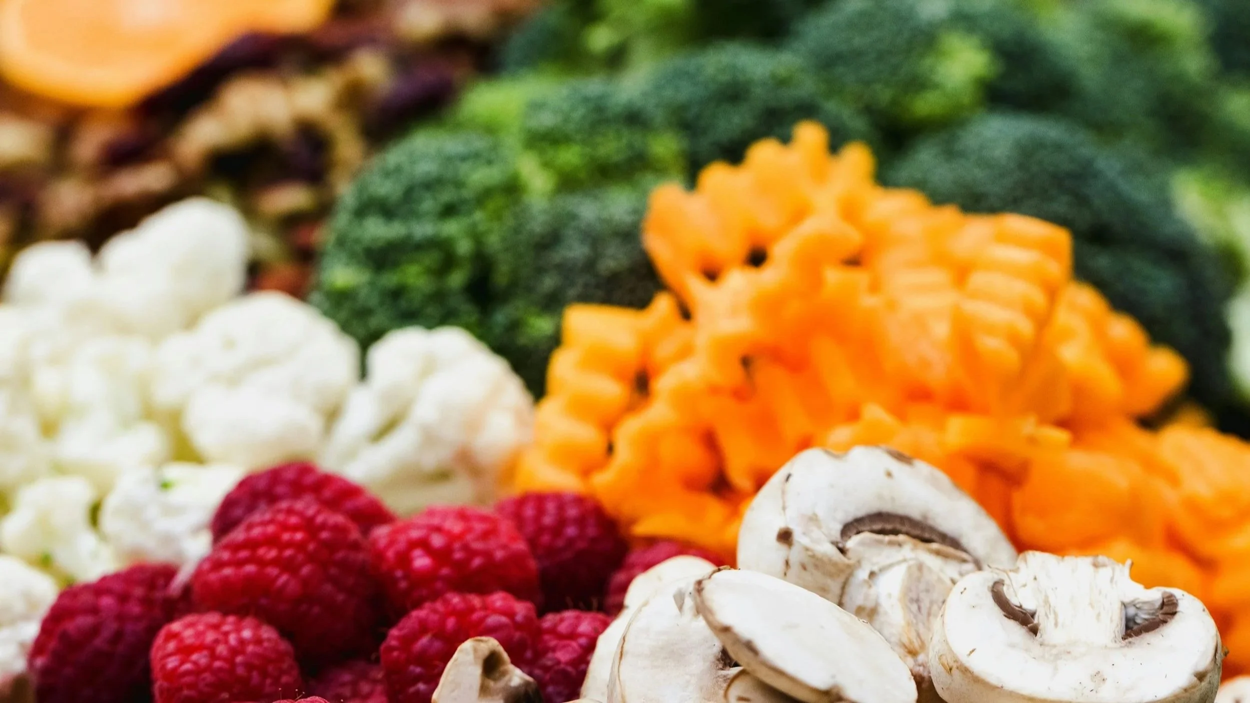 Une variété de fruits et légumes, notamment des framboises, des champignons, des brocolis, des carottes en rondelles, et d'autres légumes verts.