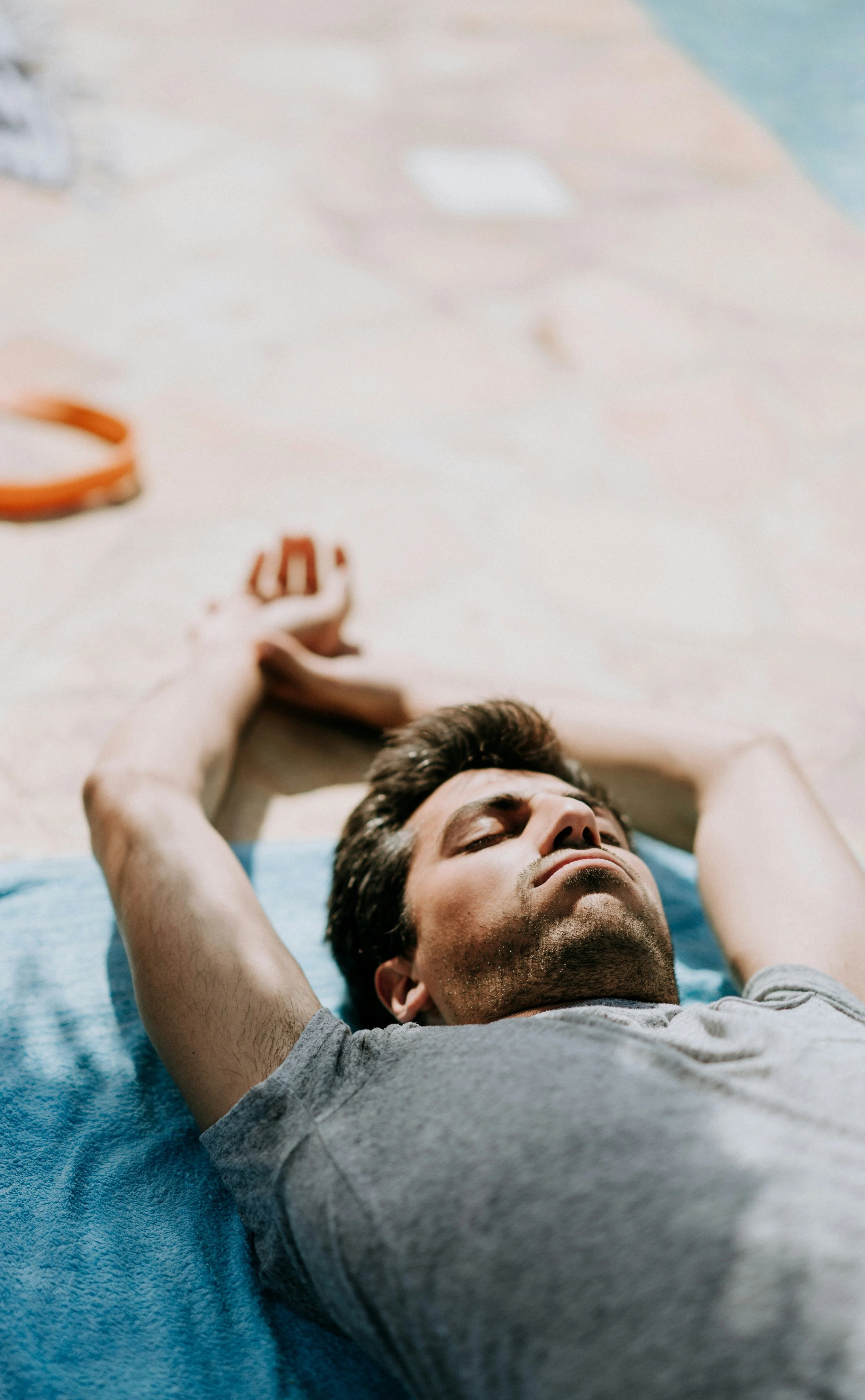 Un homme jeune, aux cheveux bruns, repose sur un tapis de yoga bleu, les bras derrière la tête, les yeux fermés, dans une position de relaxation ou de méditation.