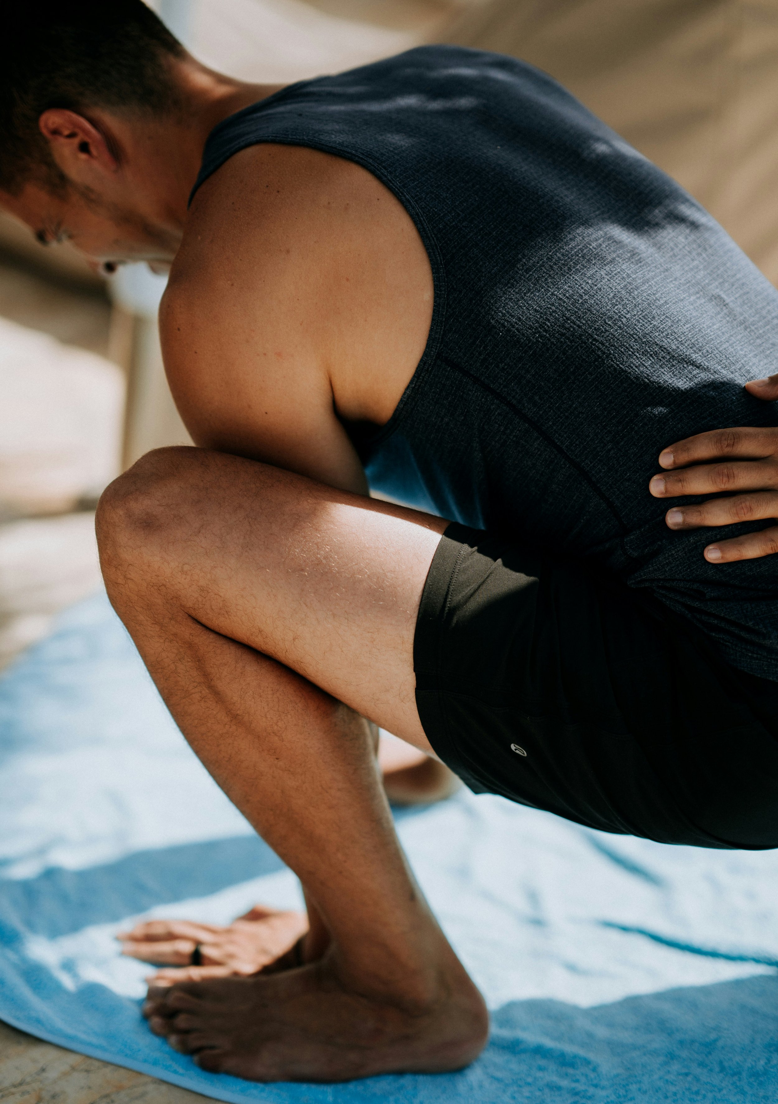 Une personne en position de yoga ou d'étirement, accroupie sur un tapis de sport, portant un t-shirt sans manches