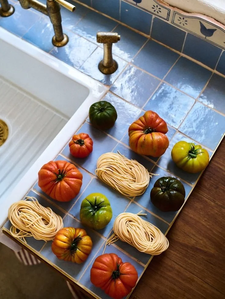 Des tomates de différentes couleurs et des petits tas de pâtes sèches sur un plan de travail de cuisine bleu, à côté d'un évier.