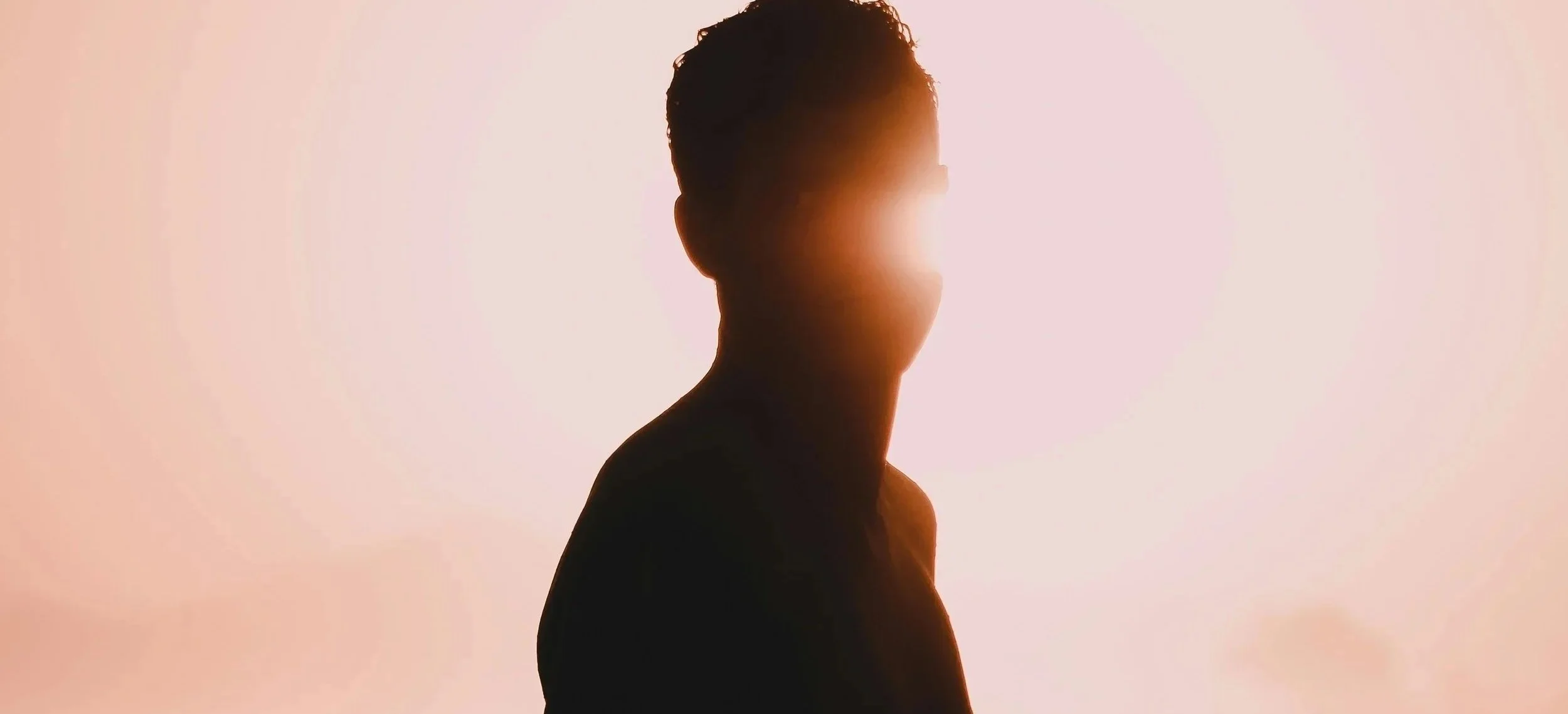 Silhouette d'une personne masculine de profil, éclairée par une lumière chaude derrière, avec un fond de couleur douce et pâle.