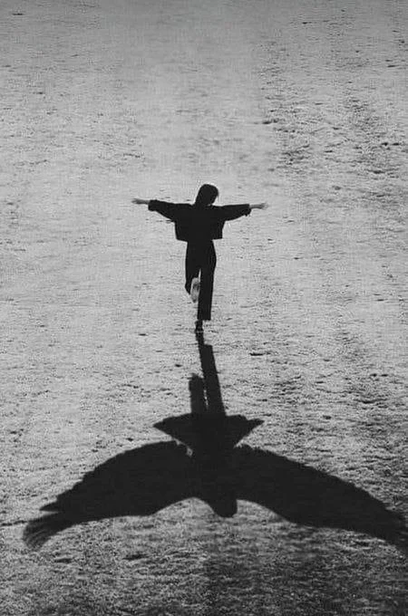 Person marchant sur un terrain plat avec ses bras étendus, créant une ombre ressemblant à un ange avec des ailes