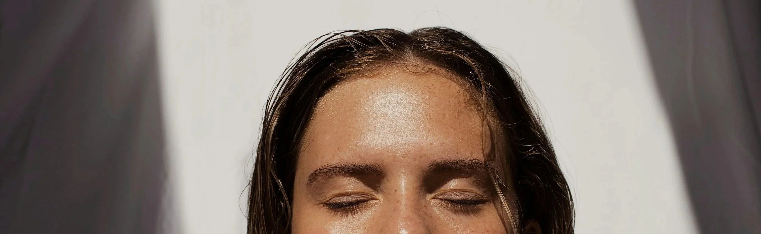 Une femme avec les yeux fermés, des cheveux mouillés, dans une lumière claire.