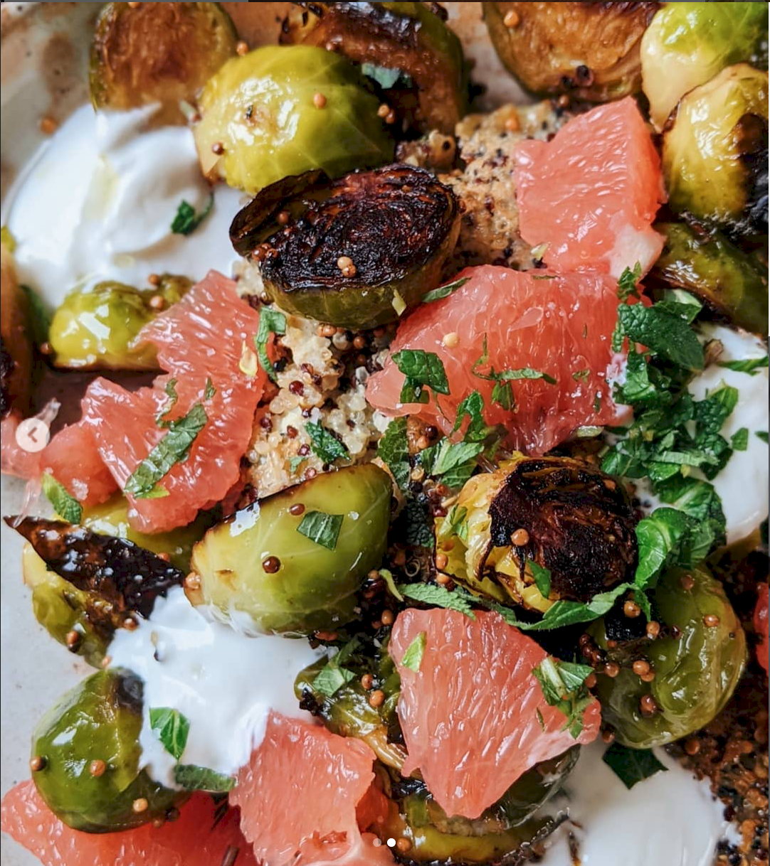 Une assiette de légumes rôtis, comprenant des brocolis, du chou-fleur, des tomates, des herbes fraîches, du yaourt ou de la sauce blanche, et des graines de moutarde.