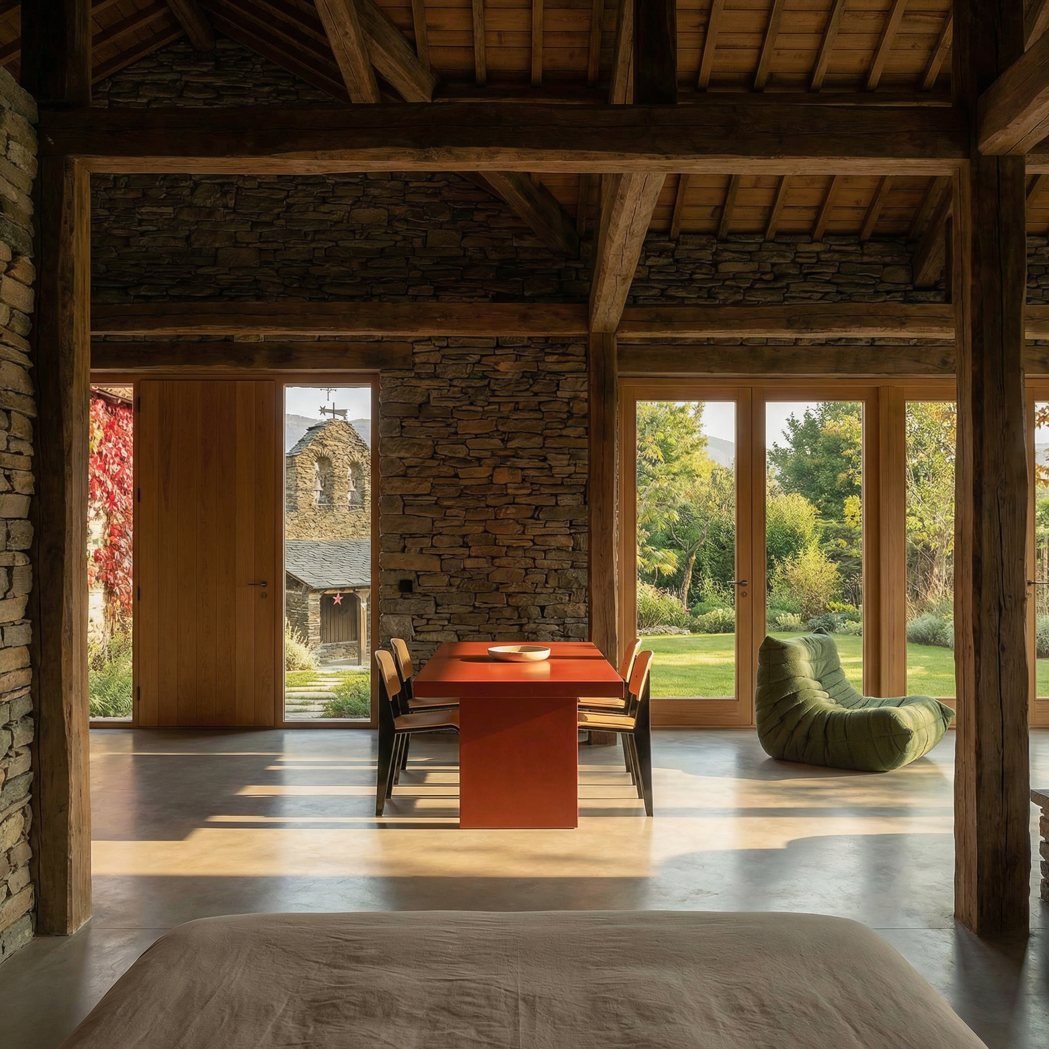 Interior rústico con paredes de piedra, vigas de madera, mesa de comedor roja, sillón verde y jardín visible por los ventanales.