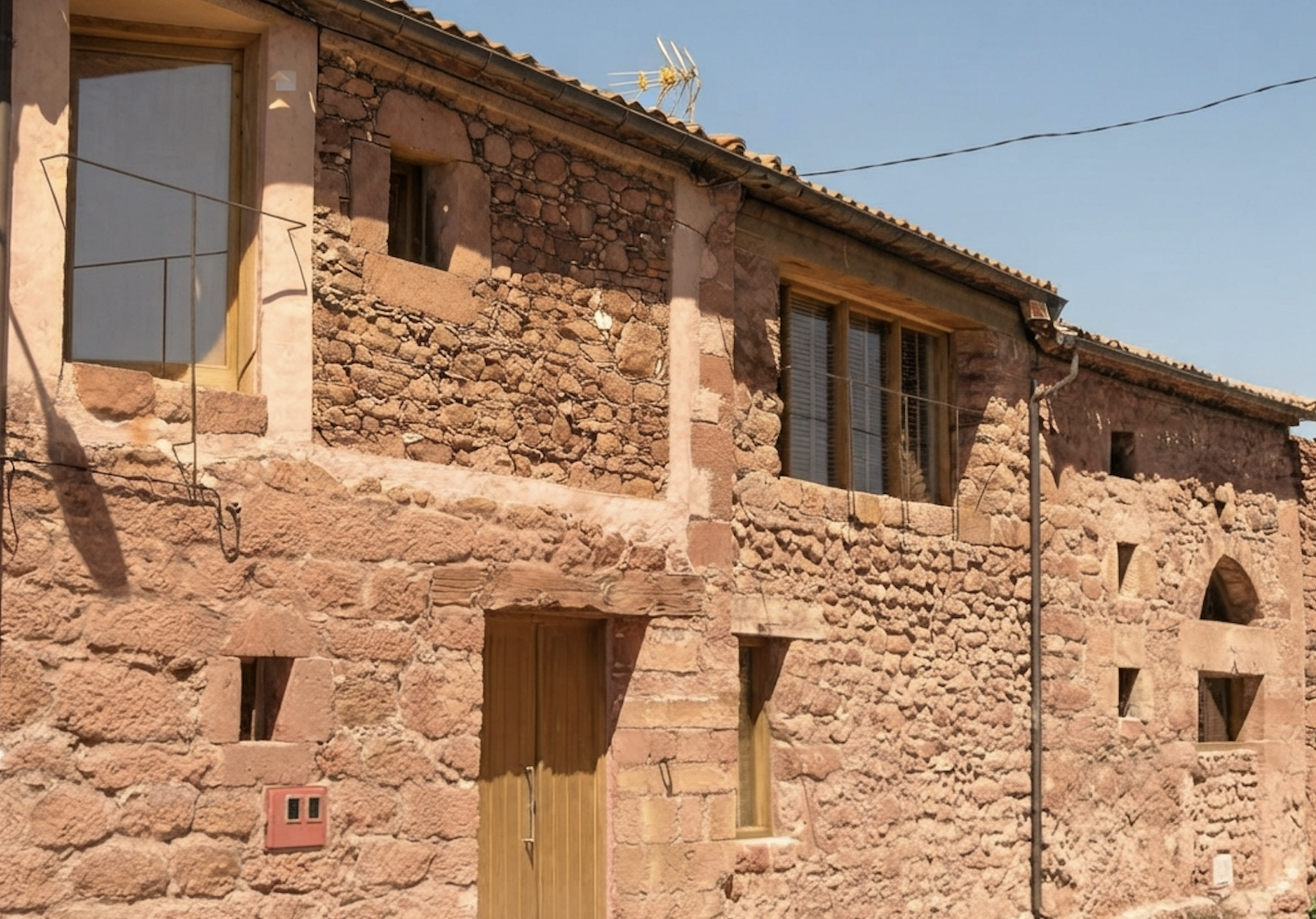 Antigua casa de piedra y adobe con puertas y ventanas de madera bajo un cielo despejado