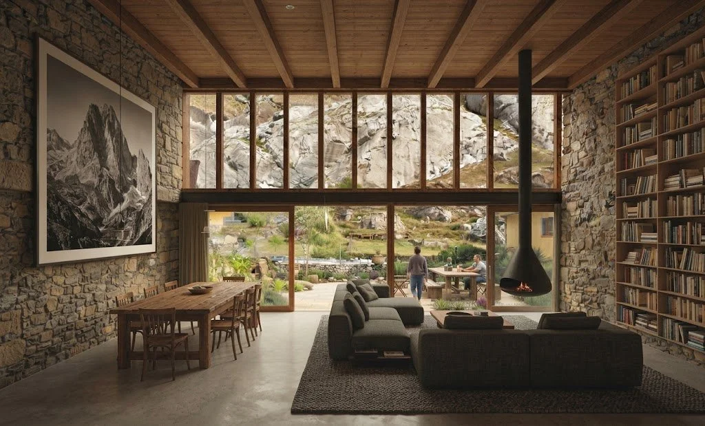 Sala rústica de piedra con biblioteca, chimenea suspendida, comedor de madera y grandes ventanales con vista a montañas rocosas.