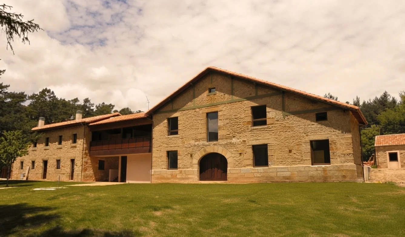 Antigua casa rural de piedra con techo de tejas, rodeada de césped y árboles.