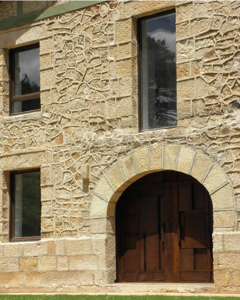 Stone building with arched wooden door and several rectangular windows.