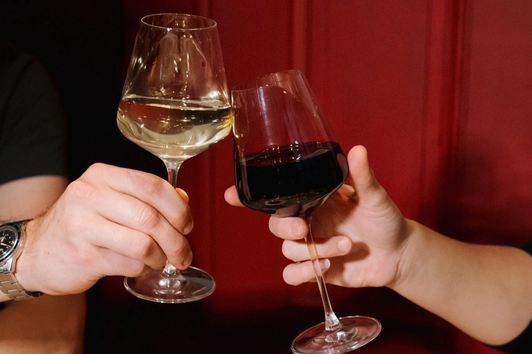 Deux personnes trinquent avec un verre de vin blanc et un verre de vin rouge.