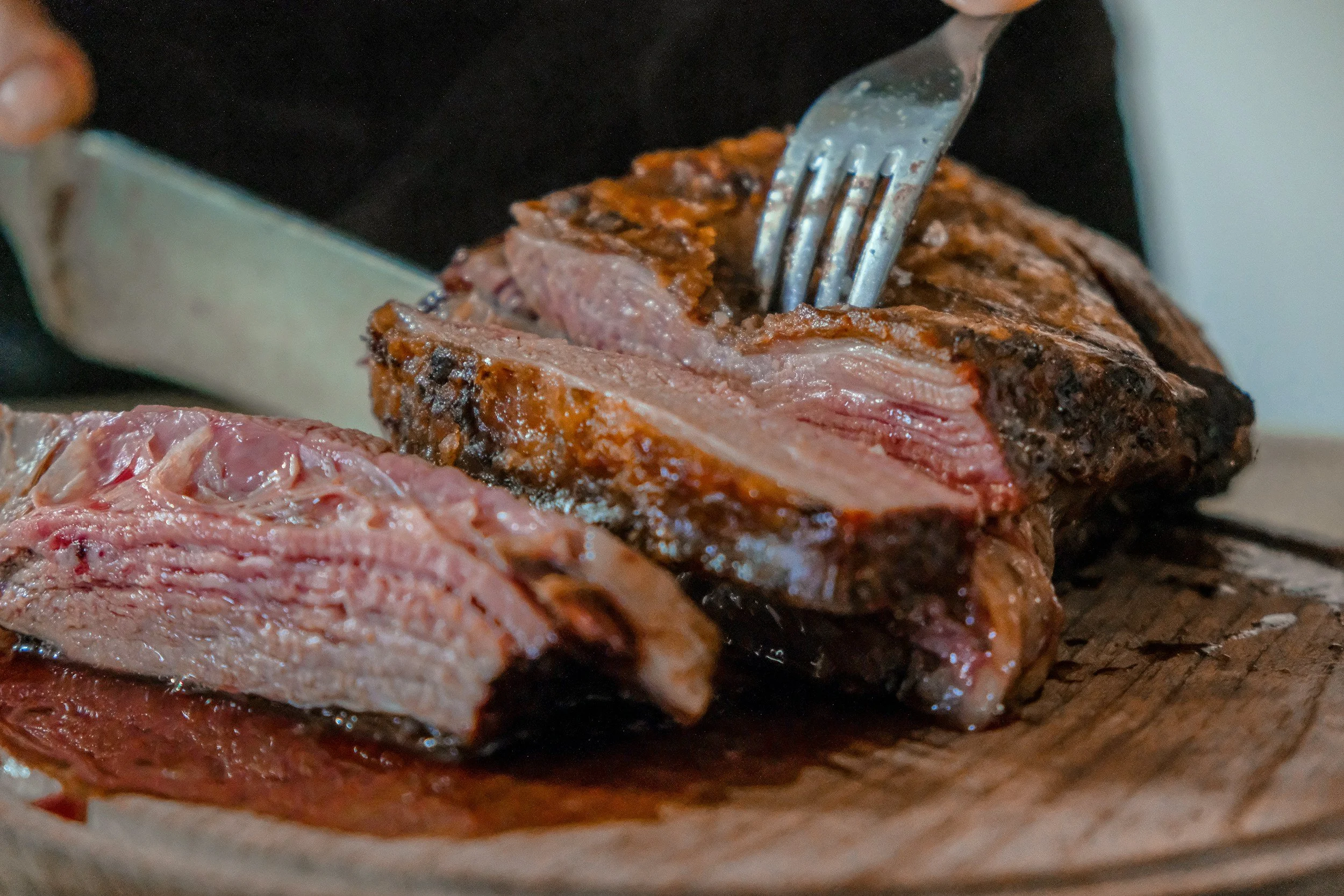 Une pièce de viande de bœuf cuite, en train d'être découpée avec une fourchette.