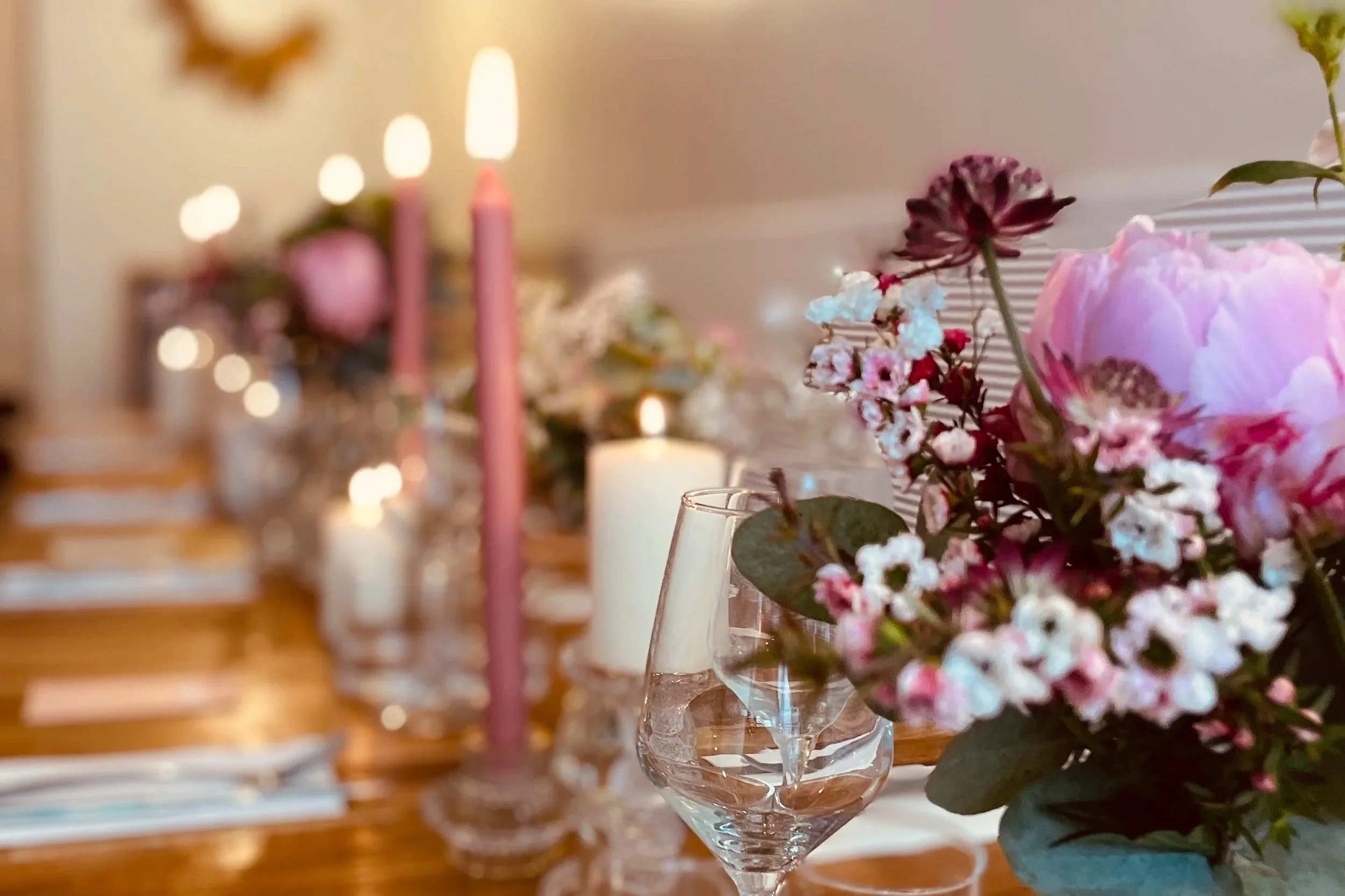 Une table décorée avec un bouquet de fleurs roses et blanches dans un vase en verre, entouré de bougies allumées dans un cadre intérieur chaleureux.