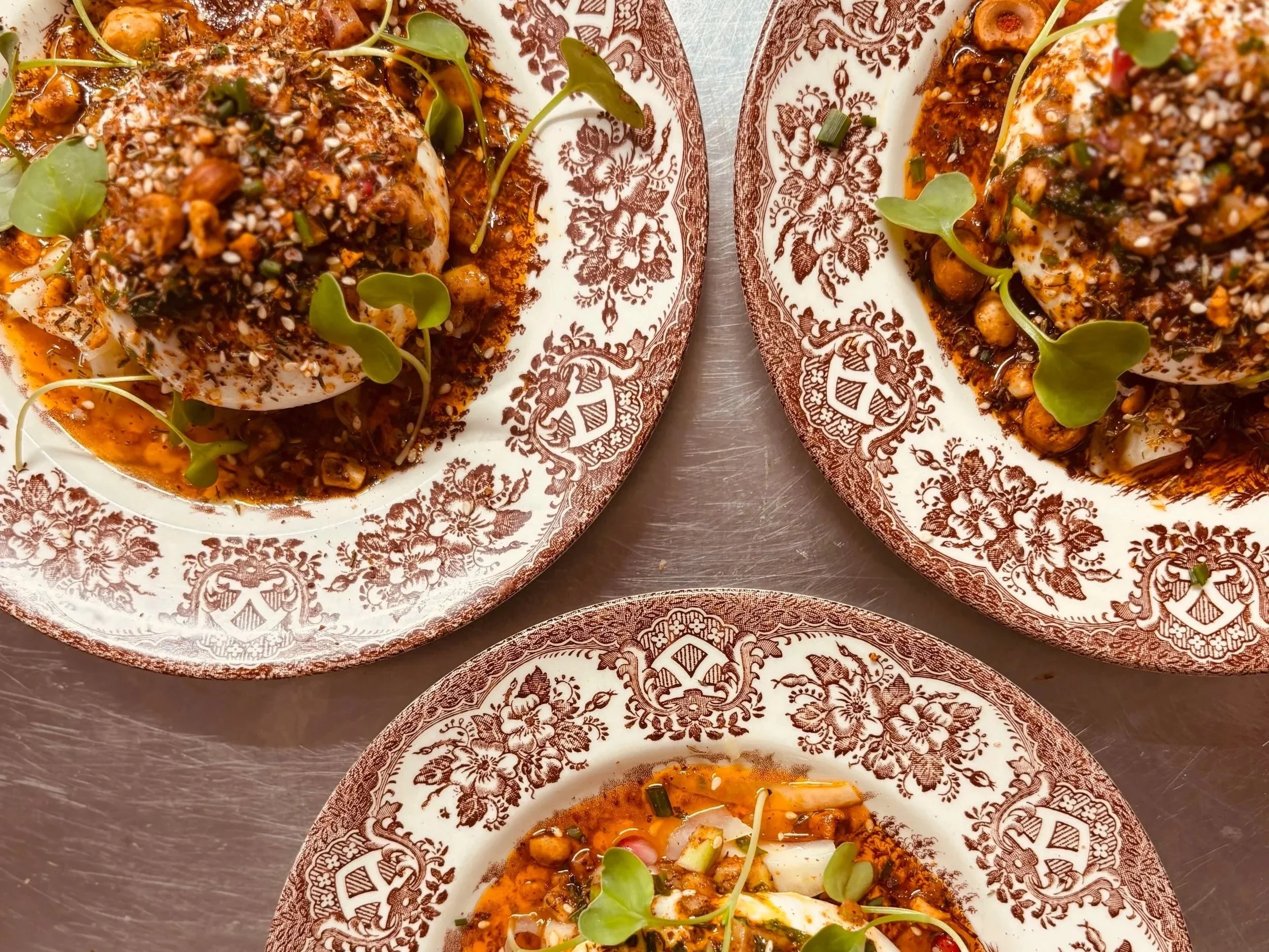 Plat avec œuf mollet, sauce rouge épaisse, graines de sésame, jeunes pousses et ciboulette sur une assiette blanche à motifs bruns.