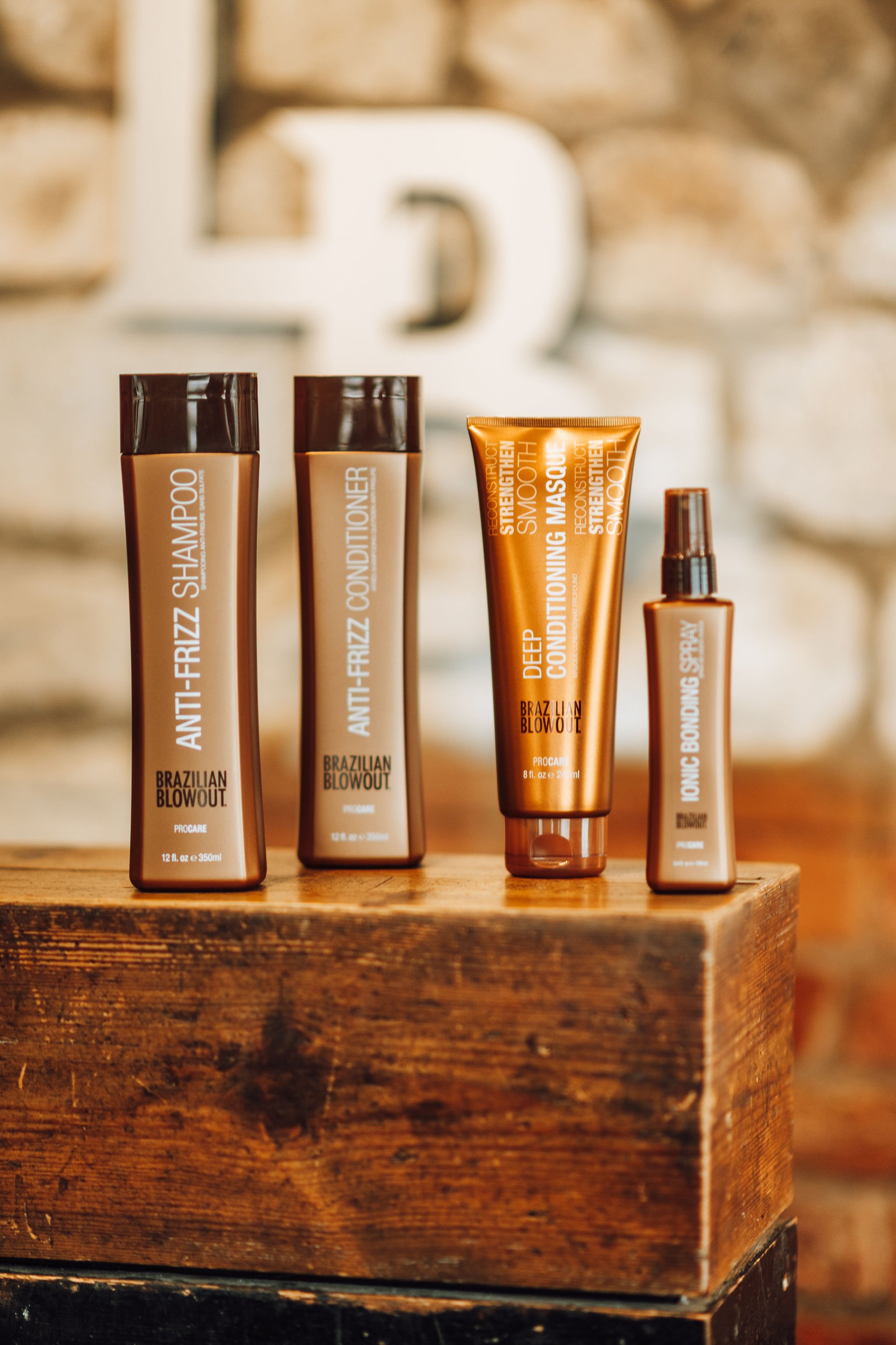 A collection of Brazilian Blowout hair care products including shampoo, conditioner, deep conditioning mask, and spray, arranged on a wooden surface.