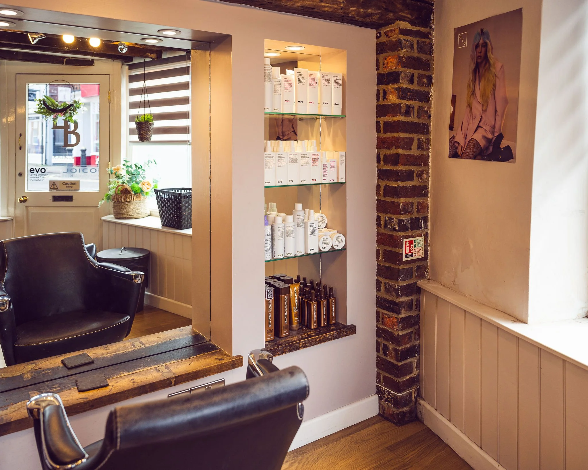 Interior of the salon showing a mirror and a black salon chair beside a wooden shelf with our hair products.