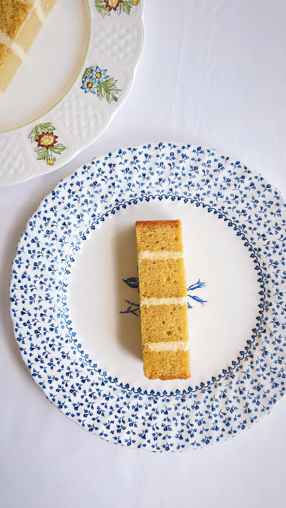 A rectangular slice of layered cake with a yellow sponge and white cream filling on a white plate with blue floral patterns.