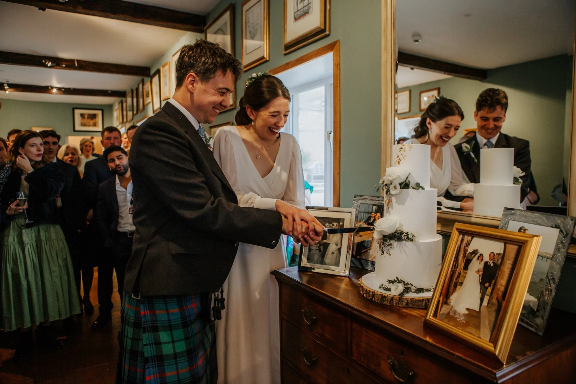A wedding celebration with a man and woman in formal attire smiling and holding hands around a table filled with framed photos and floral arrangements.