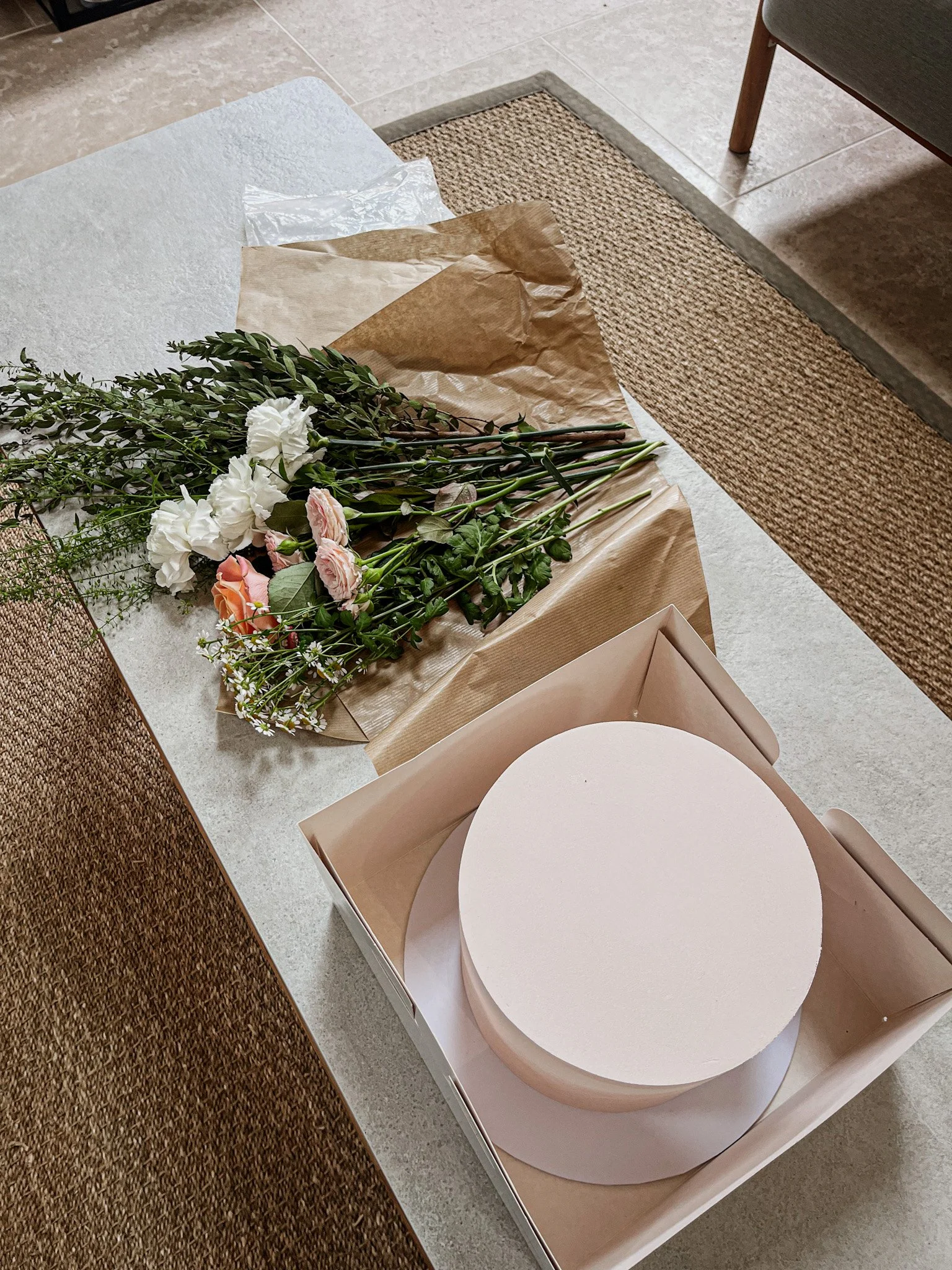 A table with a bouquet of mixed flowers wrapped in brown paper. The bouquet includes white, pink, and peach flowers with green foliage.