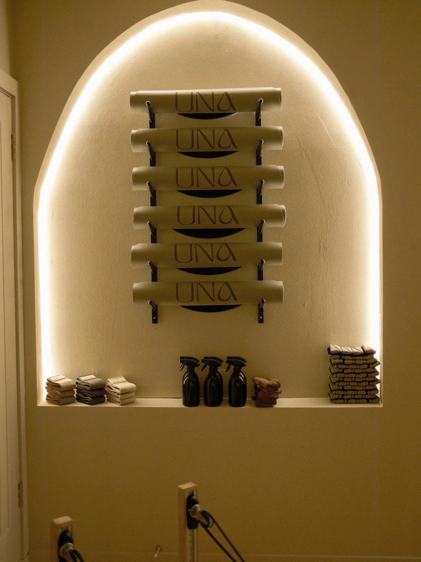 Display of folded towels and bottles of cleaning supplies on shelves, with a large wall sign spelling 'UNA' in the background.