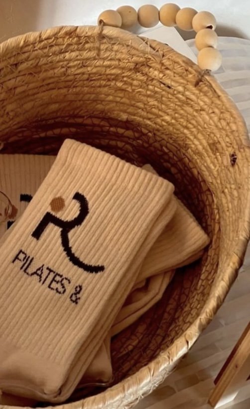 A woven basket containing folded beige fabric with the letters 'RL' and the words 'FILES 4' embroidered on it, and a wooden beaded handle on top.