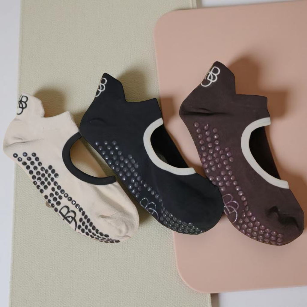 Three athletic shoe insoles in white, black, and brown, with textured grips on the bottom, placed on a surface next to a pink mat.