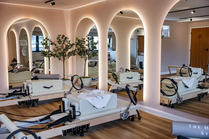 A Pilates or physical therapy studio with multiple reformer machines, mirrors, indoor plants, wooden floors, and a minimalist décor.