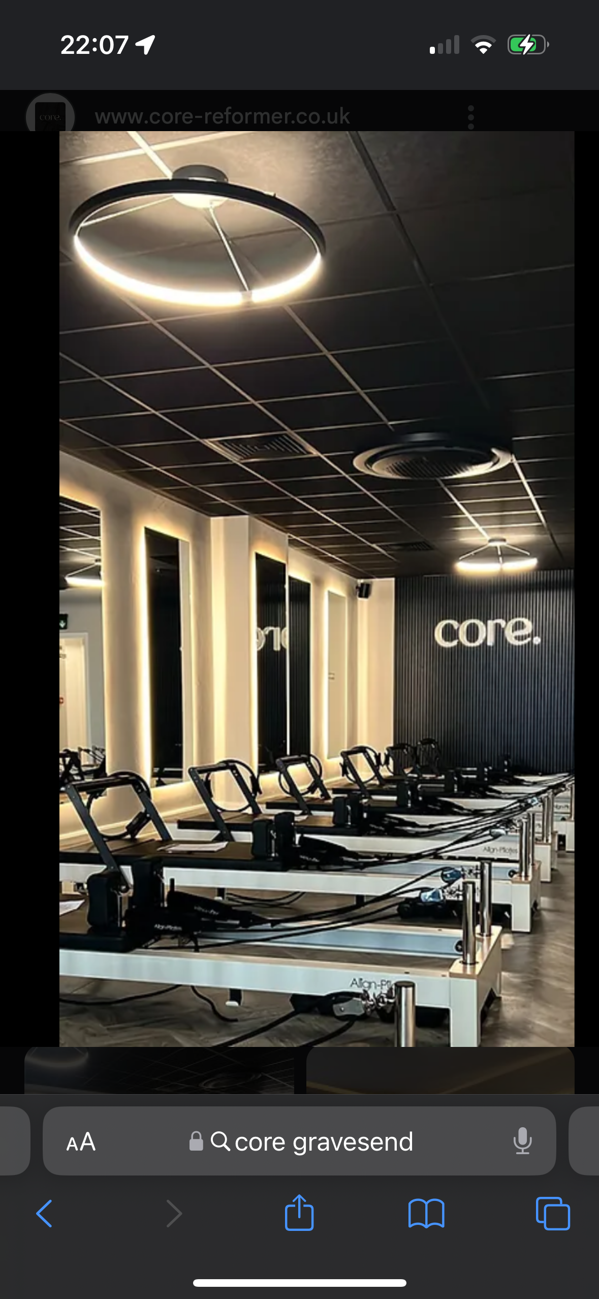 Exercise studio with reformer machines lined up, illuminated mirrors, modern lighting fixtures, and a black textured wall with the word 'core.'