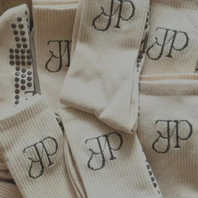 Multiple cream-colored socks with a black embroidered monogram 'JP' on the side, some in focus and others slightly bunched together.
