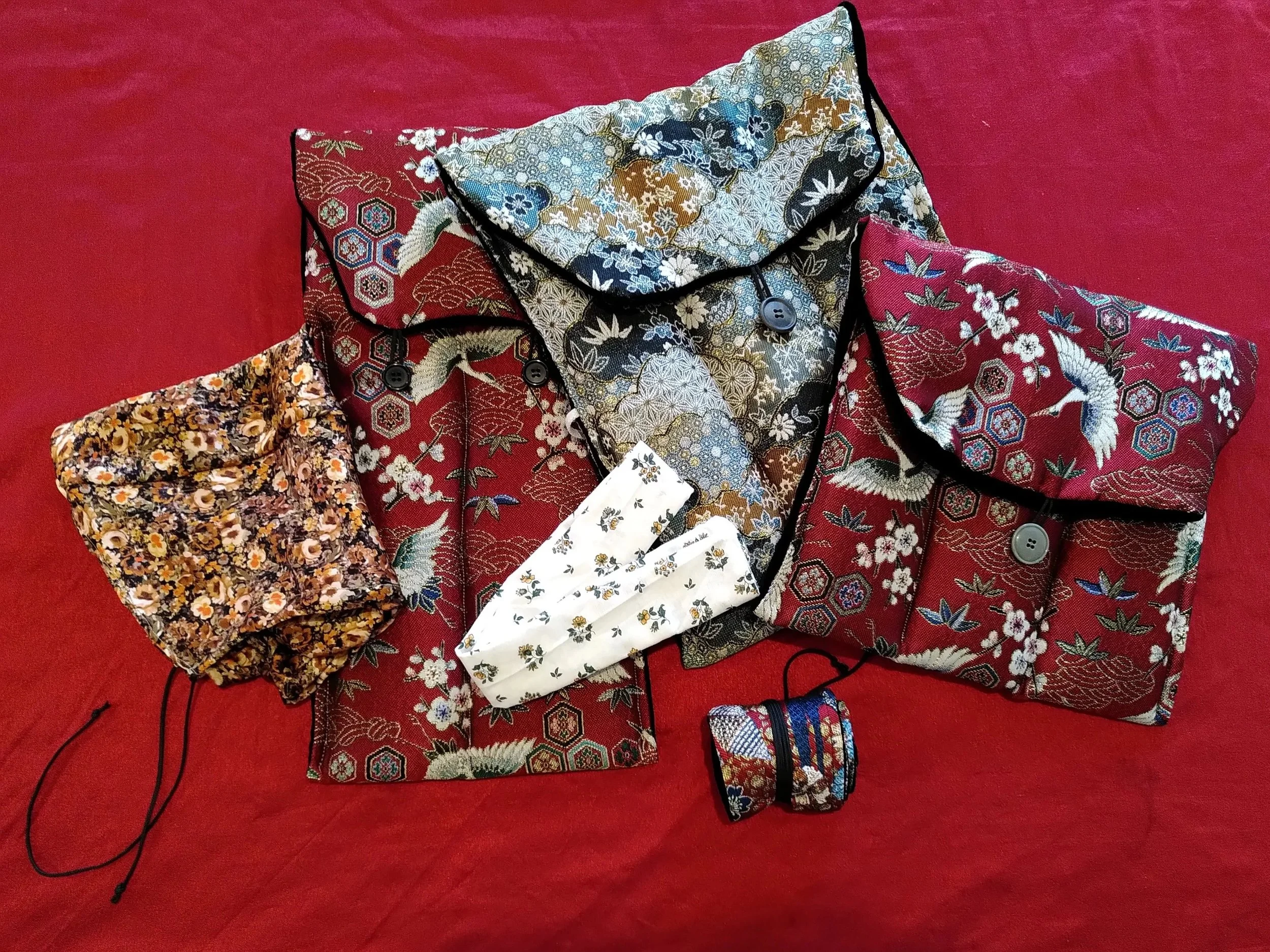 Vêtements asiatiques en tissu brodé avec des motifs floraux, oiseaux et formes géométriques, disposés sur un fond rouge.