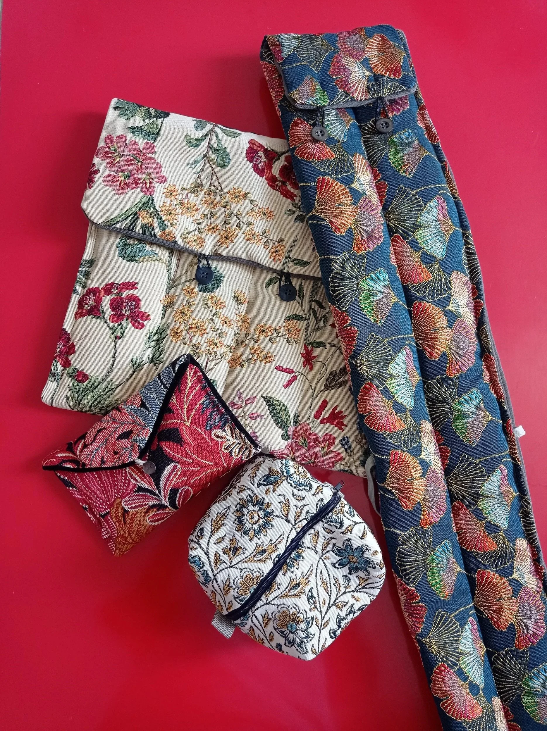 Différentes pochettes et une longue bande de tissu en tissu brodé avec des motifs floraux et de papillons, sur un fond rose.