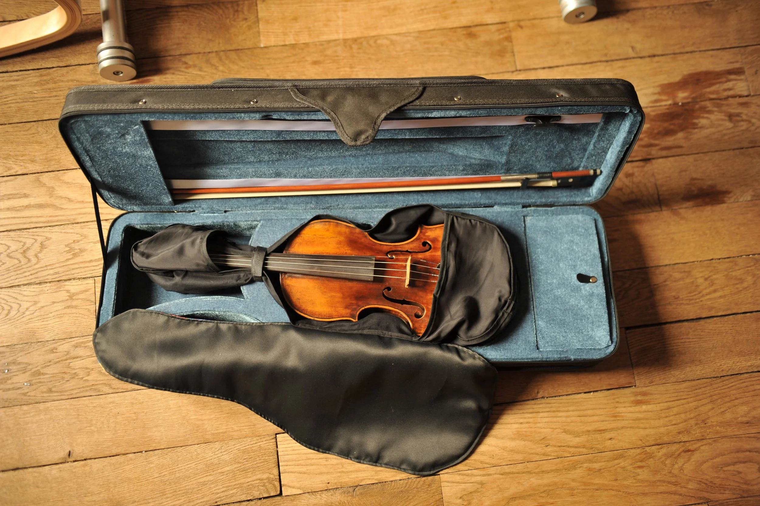 Une violon dans une boîte de rangement noire avec un étui, posée sur un sol en bois.