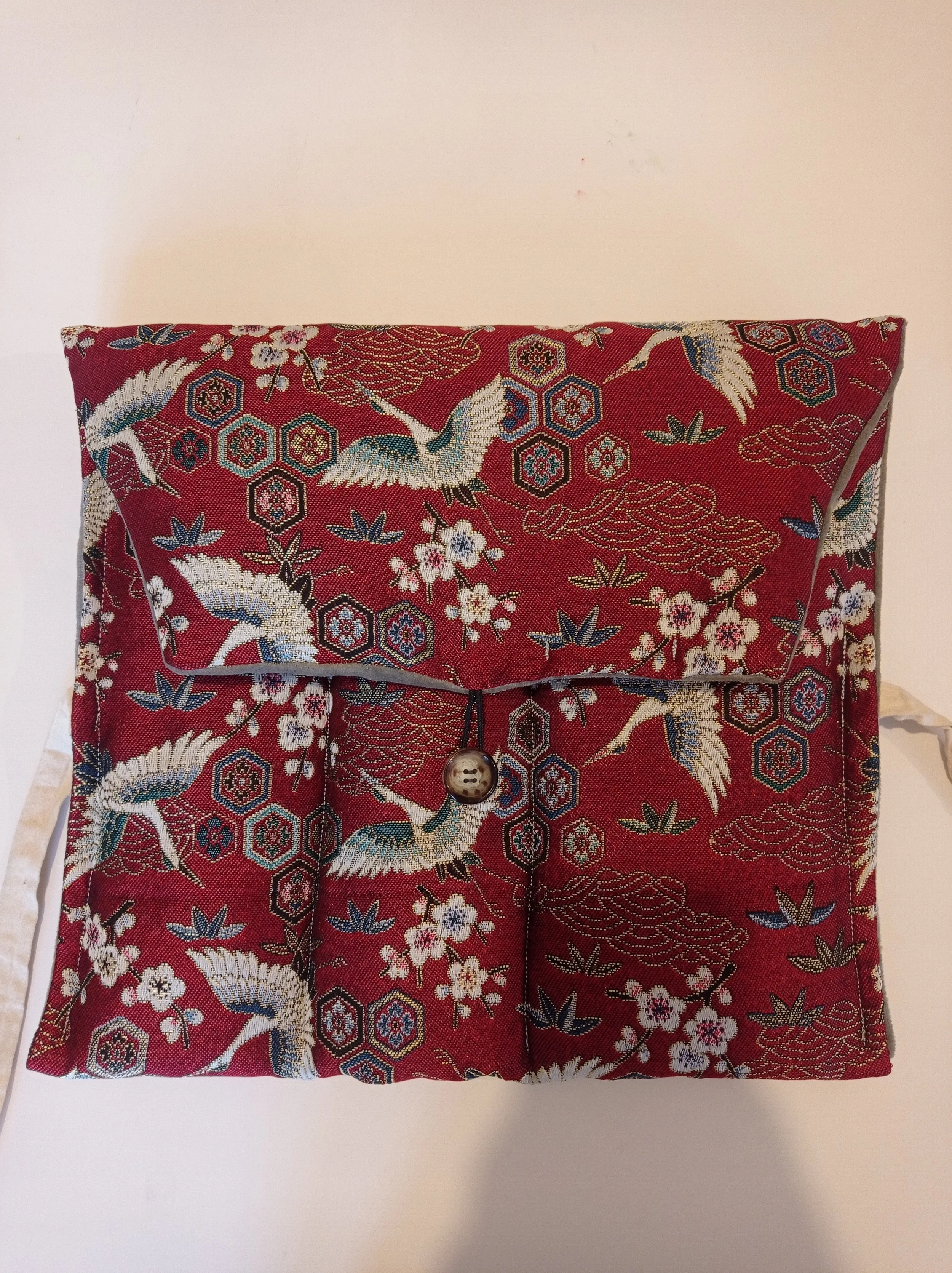 Une broderie devant un fond blanc, représentant des grues, des fleurs et des motifs hexagonaux rouges, bleus, blancs et verts sur un tissu rouge.
