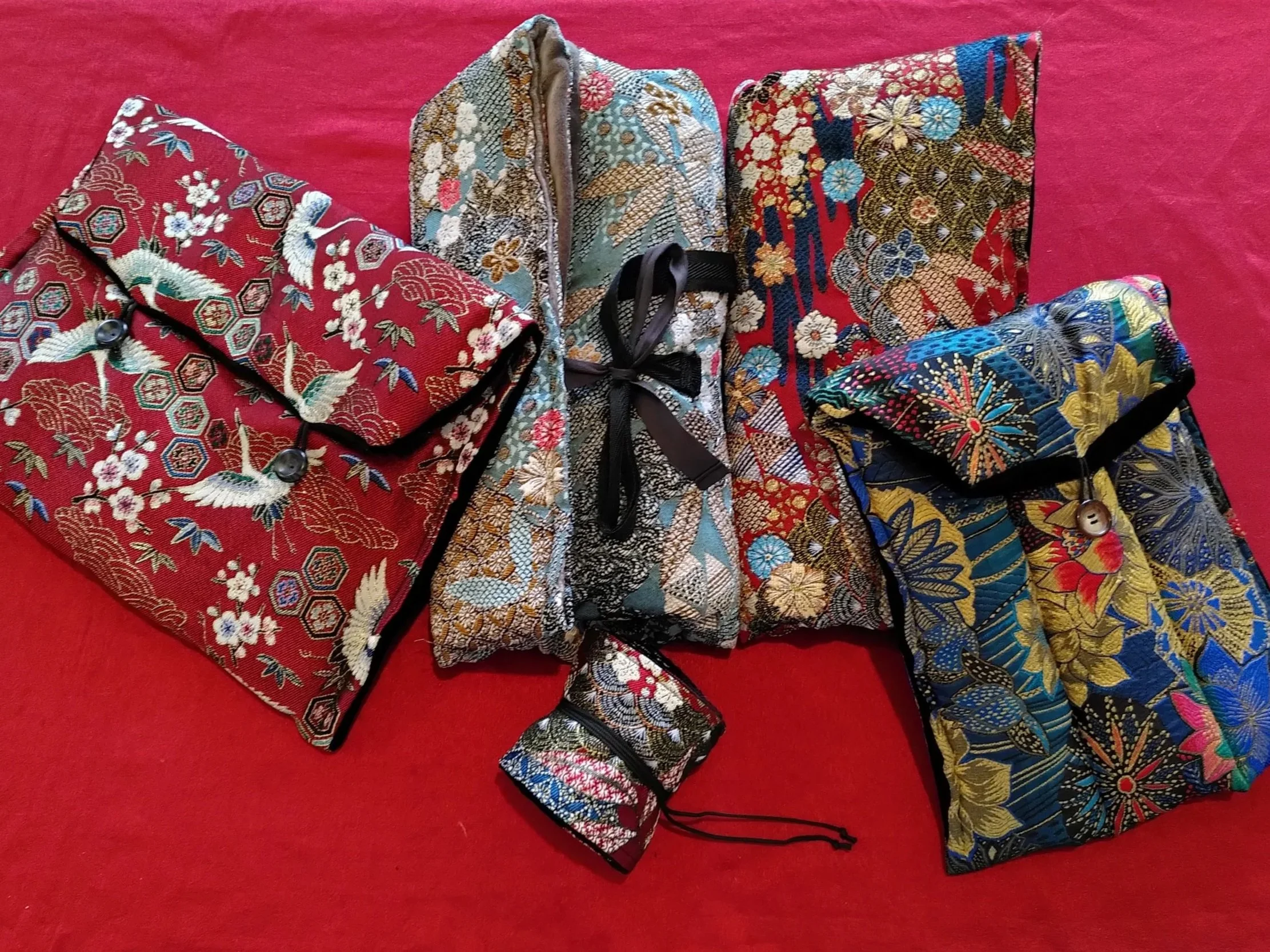 Cinq sacs ou pochettes en tissu avec des motifs japonais traditionnels, posés sur un fond rouge.