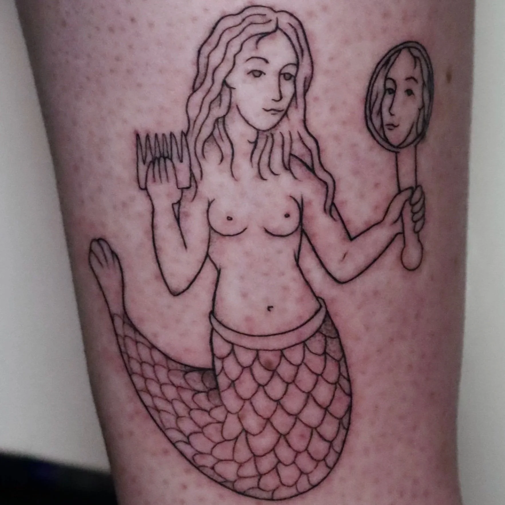 Fineline tattoo of a mermaid holding a comb and mirror, classical illustration style