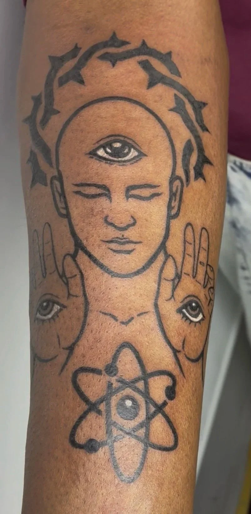 Blackwork tattoo of a third-eye figure with crown of thorns, eyes on palms, and atom symbol, surreal spiritual symbolic design
