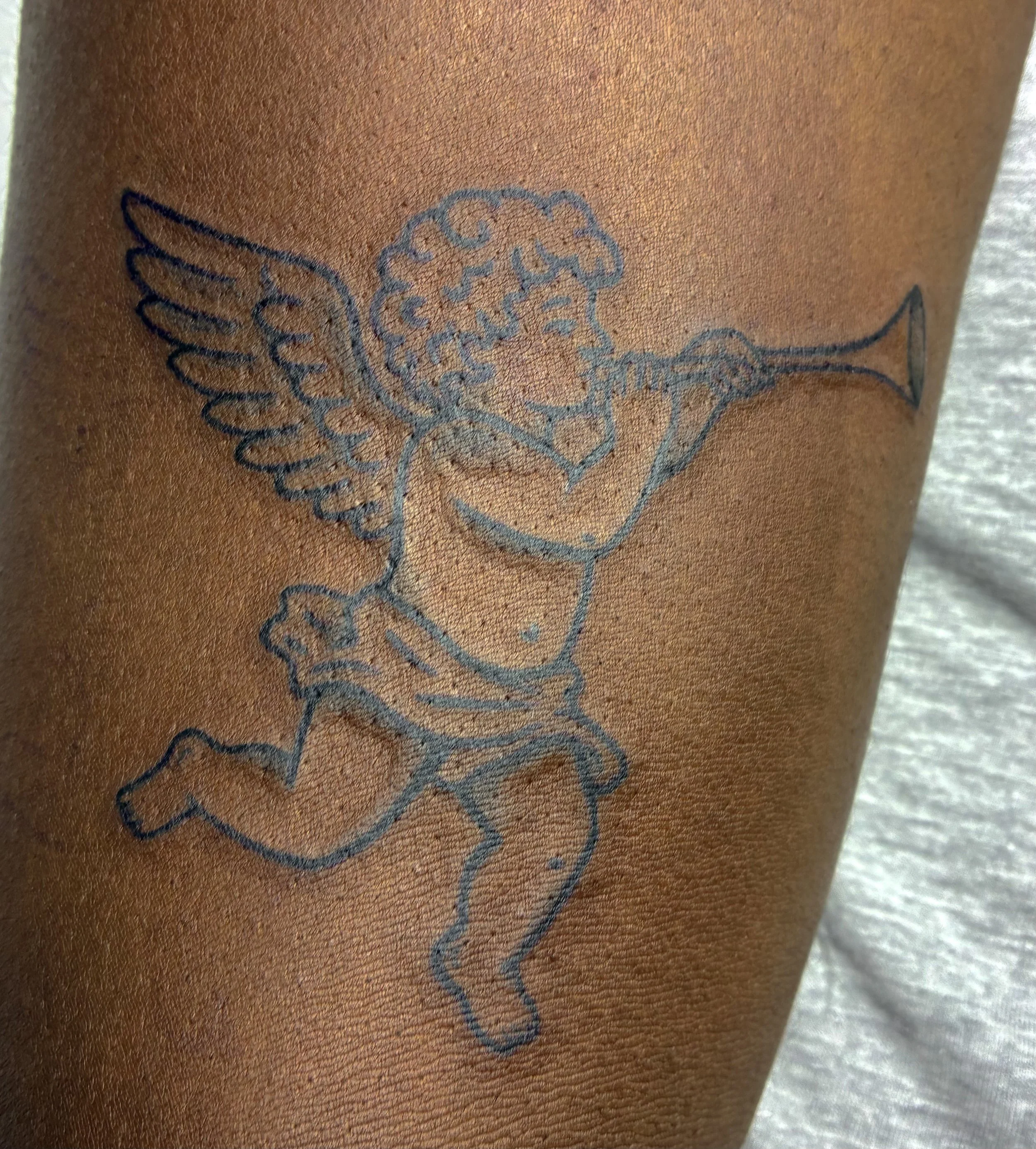 Fineline tattoo of a cherub angel playing a trumpet, classical illustration style
