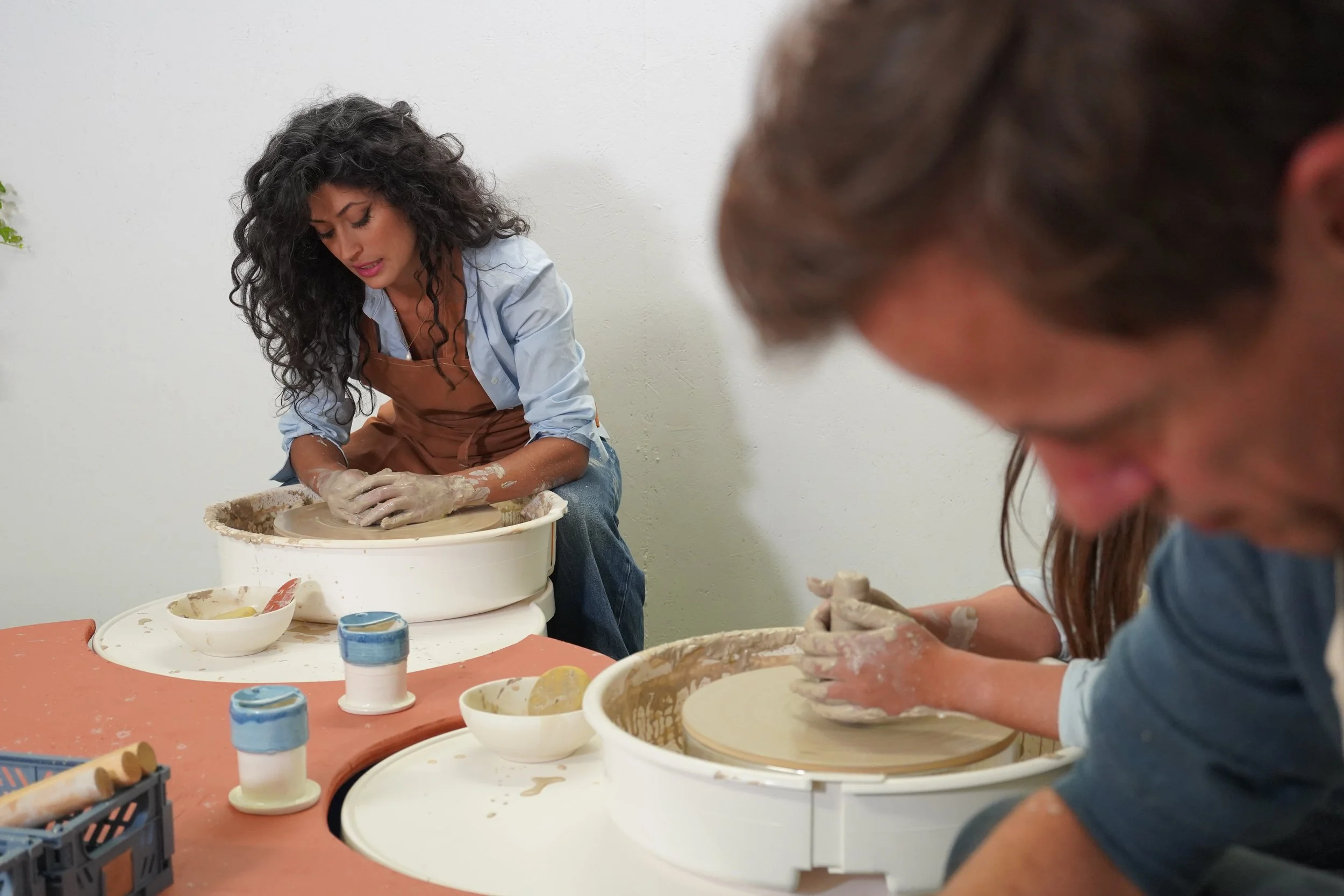 Two women working at pottery wheels, shaping clay during a pottery class or workshop.