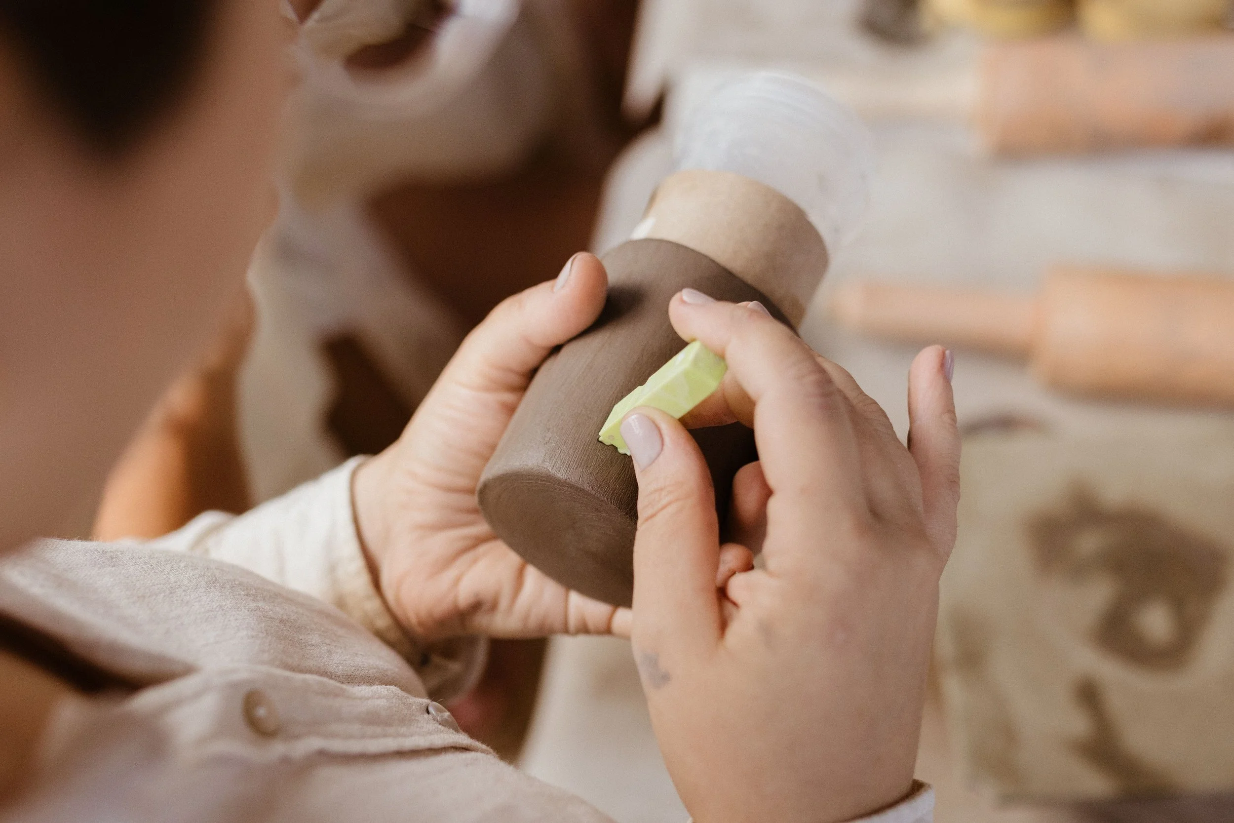 Close-up of a person carving a wooden object with a small chisel and a yellow file.