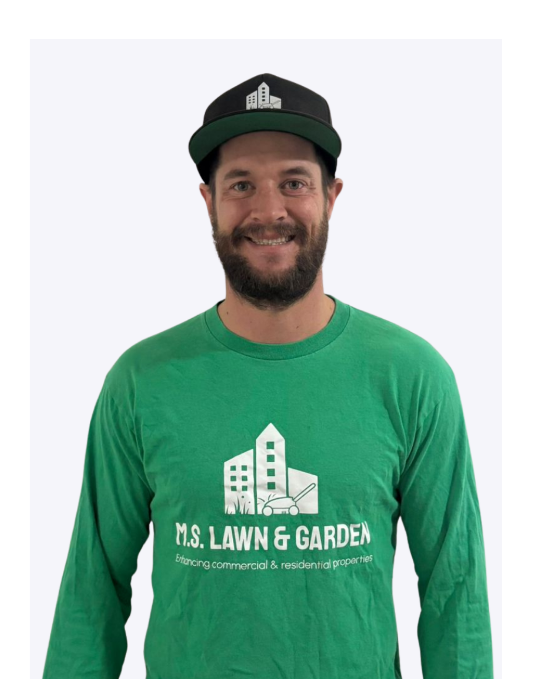 Smiling man wearing a green long sleeve shirt and a black cap with a cityscape logo, standing against a plain background.