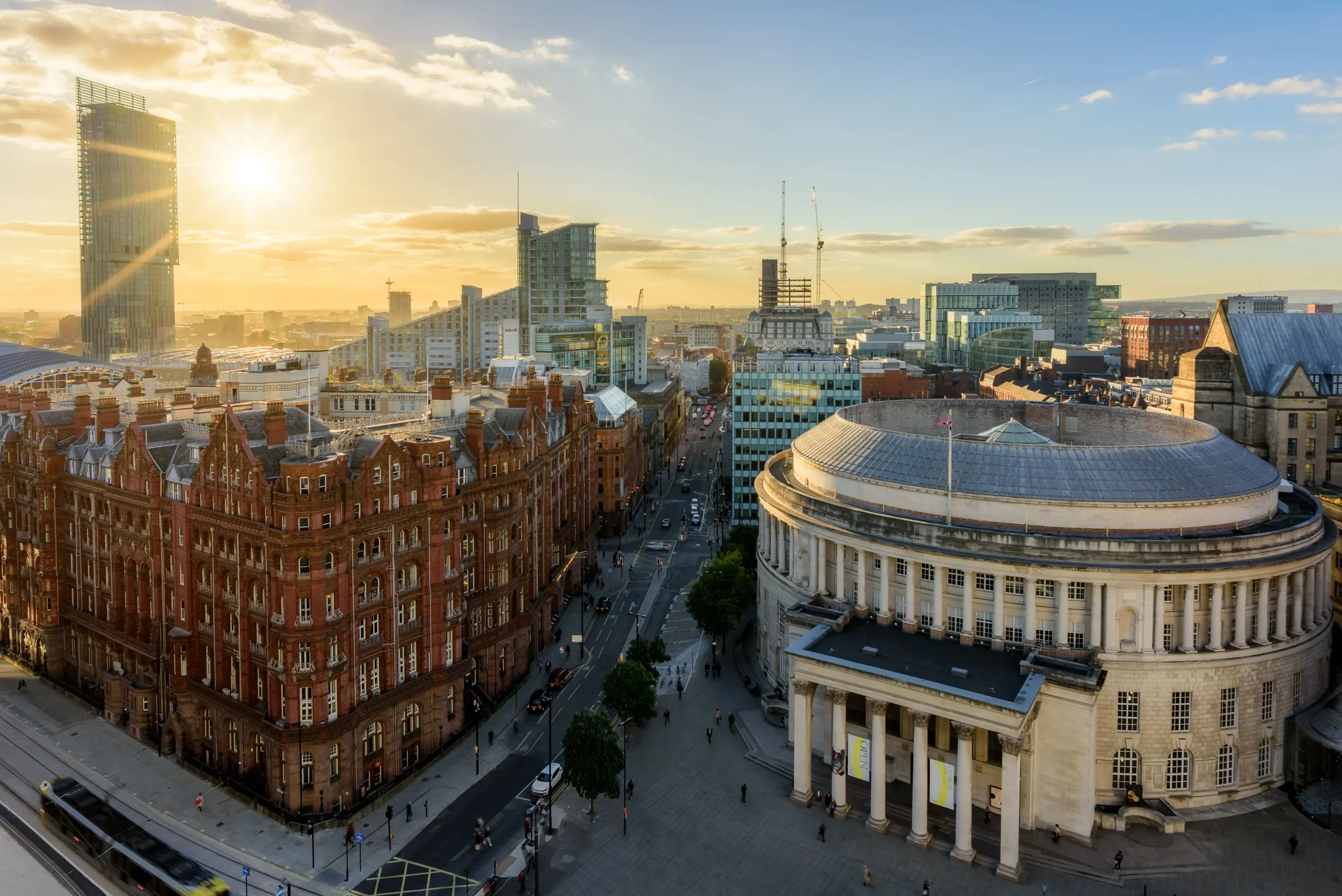 Cityscape view of a modern downtown area during sunset, with tall glass buildings, older brick buildings, and a prominent white courthouse with columns in the foreground.