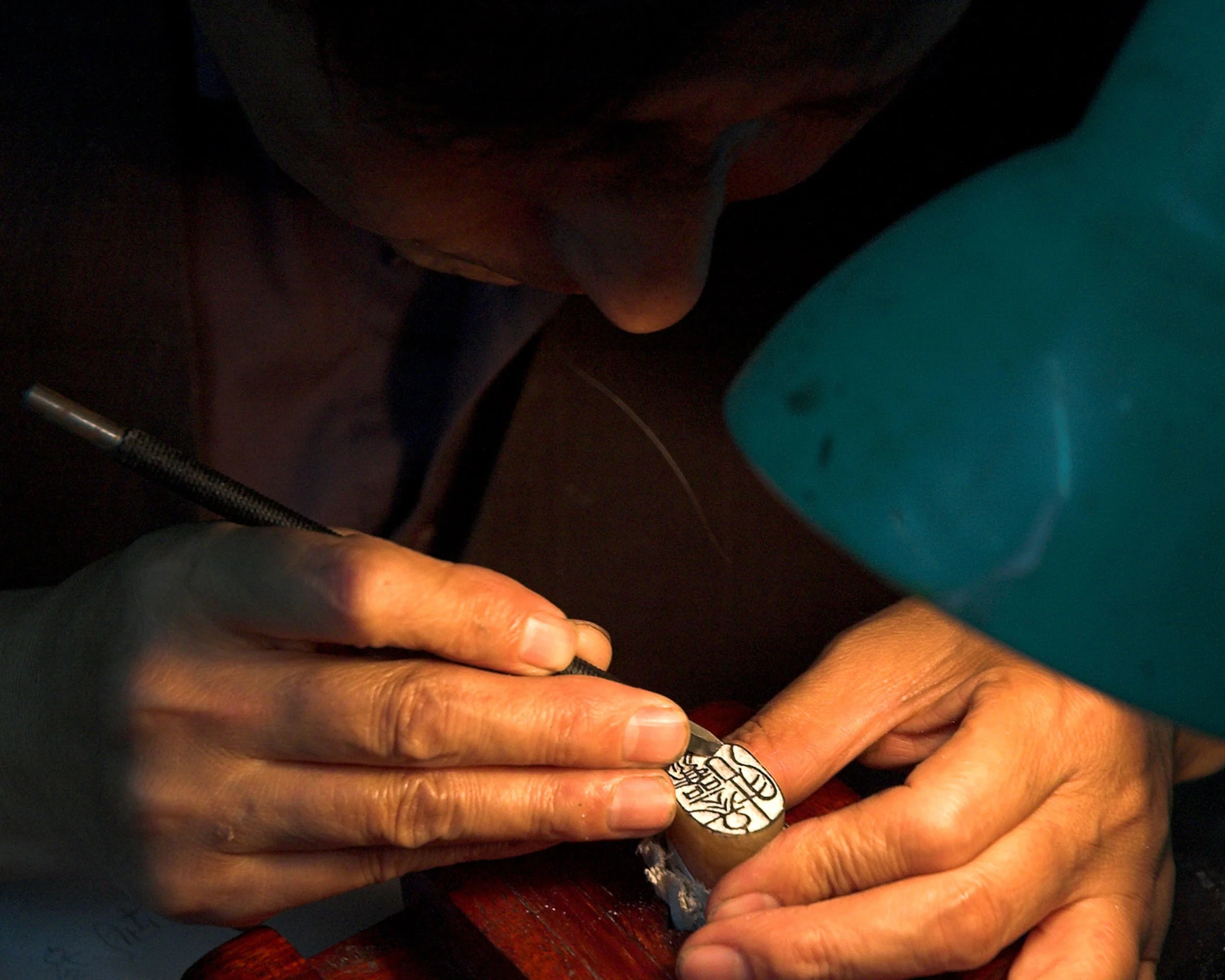 Close-up of a person's hands, one with a silver ring with an intricate design, holding a small object with a black and white calligraphy in a dark setting. Chengdu, China