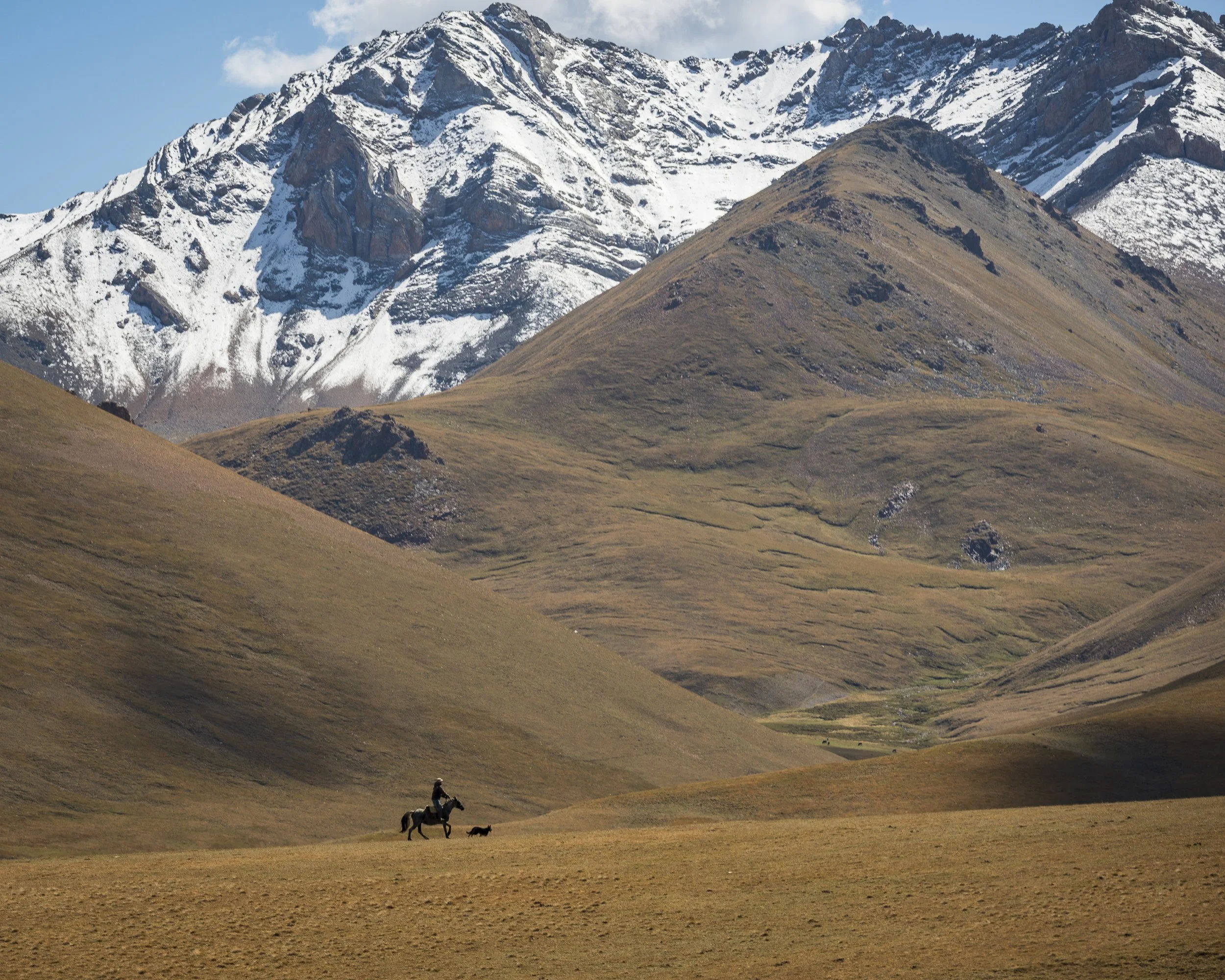 A lone horseman and his dog traverse the high peaks near Son Kul
