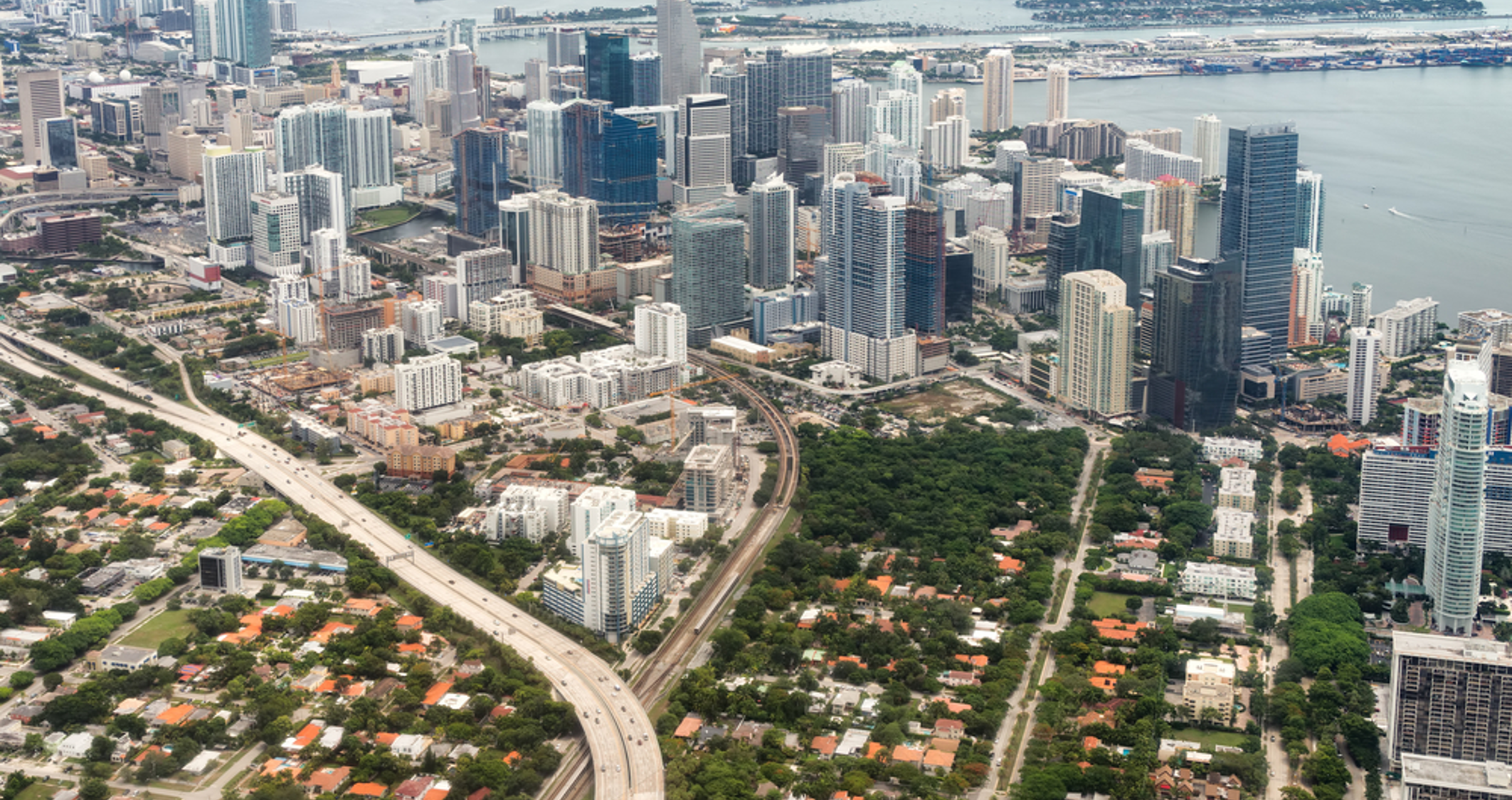 Aerial view of Brickell and The Roads neighborhoods in Miami, with high-rise buildings and tree-lined residential streets.